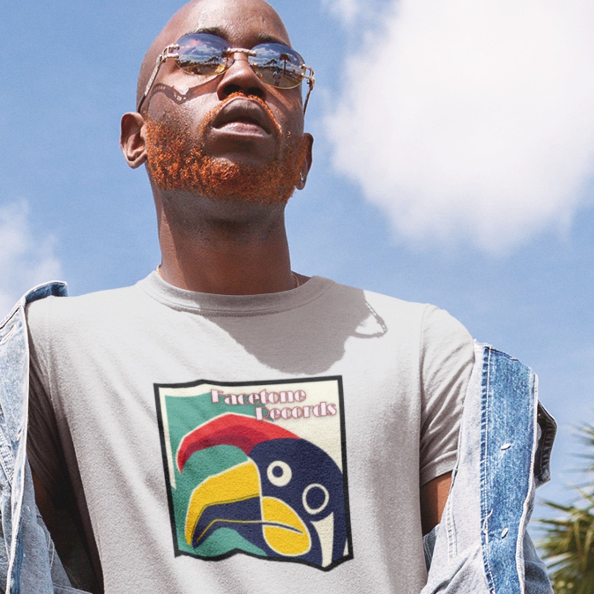 Man wearing a t-shirt with a colorful graphic design against a blue sky.