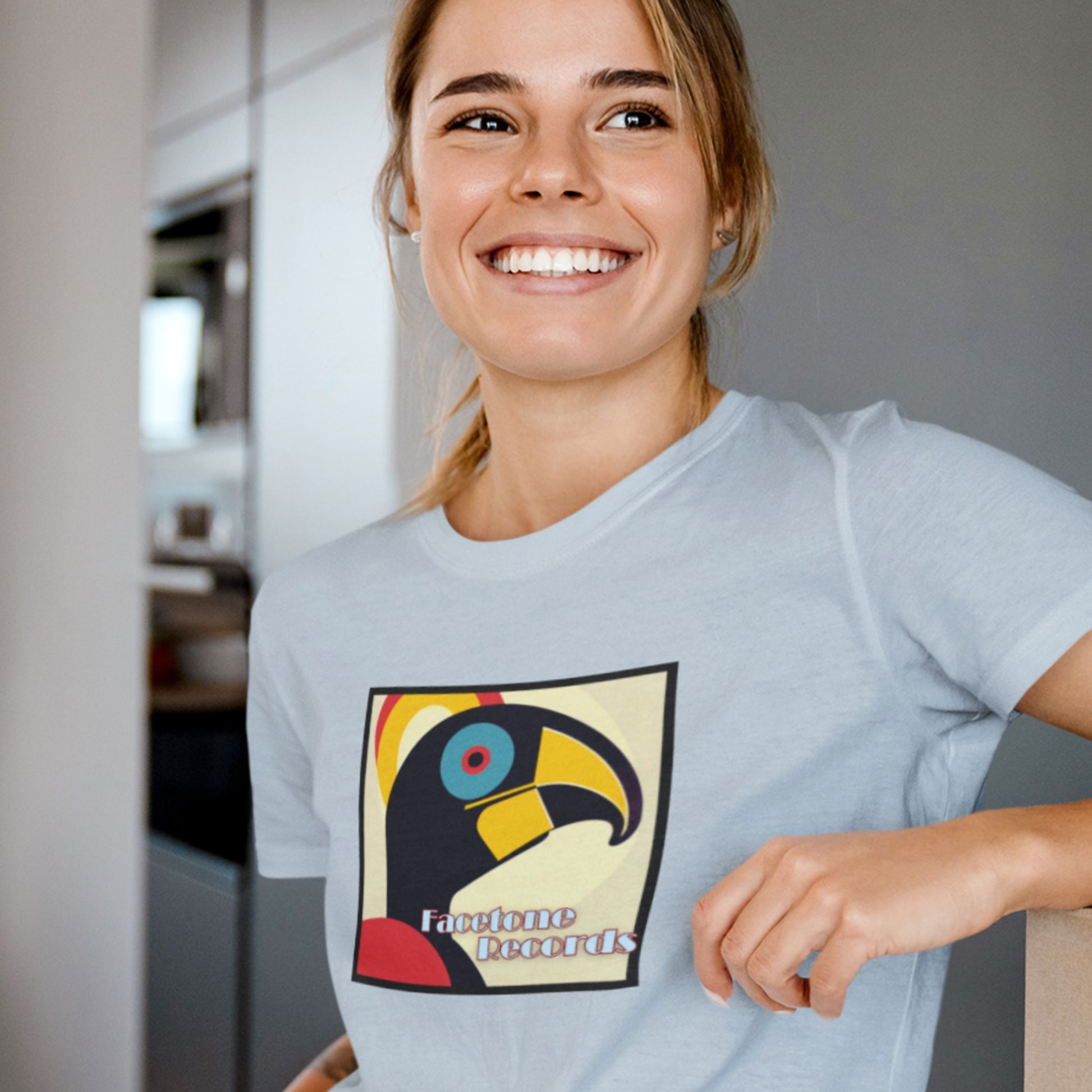 Woman wearing a light blue t-shirt with a colorful graphic hornbill design in a kitchen setting