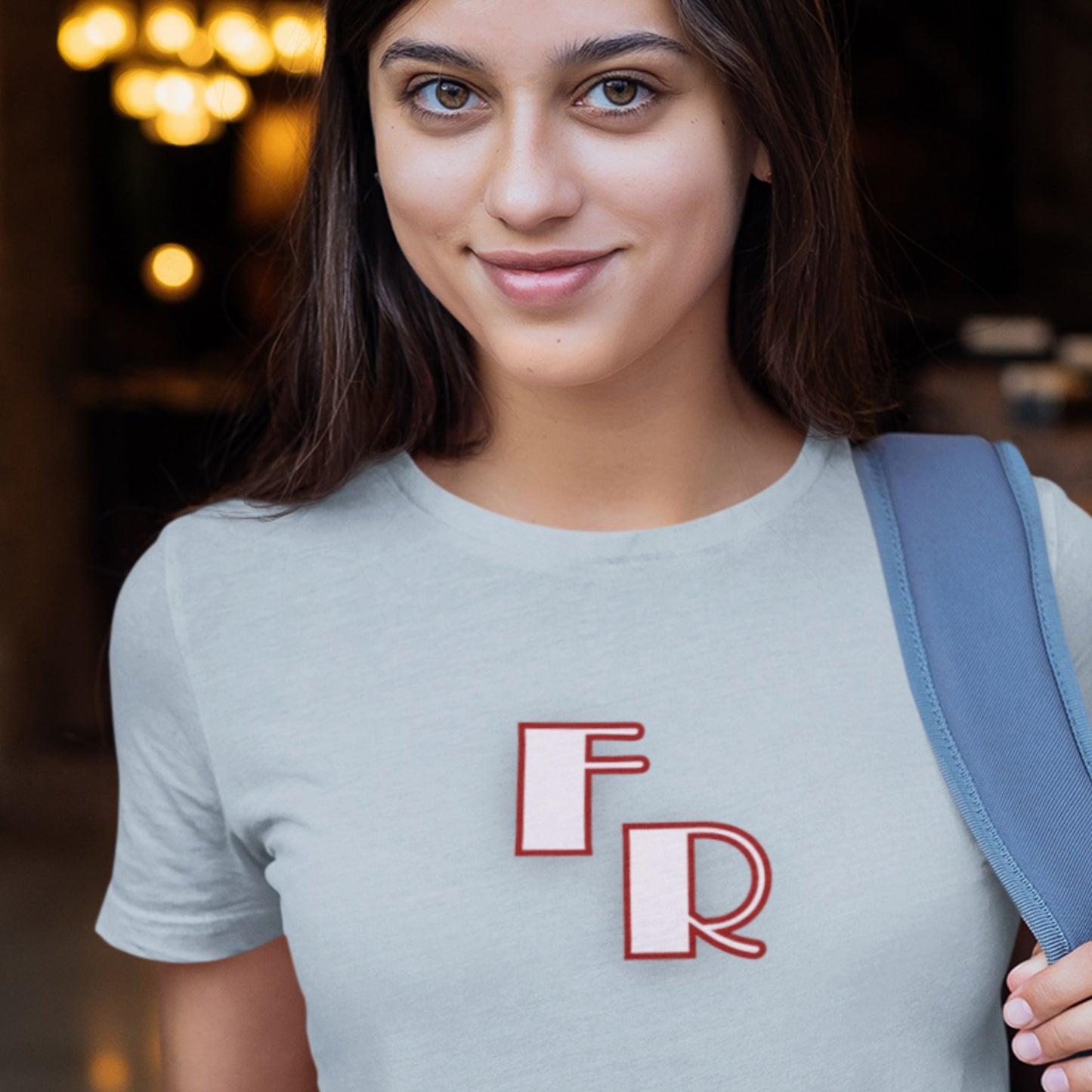 Woman wearing a gray t-shirt with 'FR' on it, holding a blue backpack.