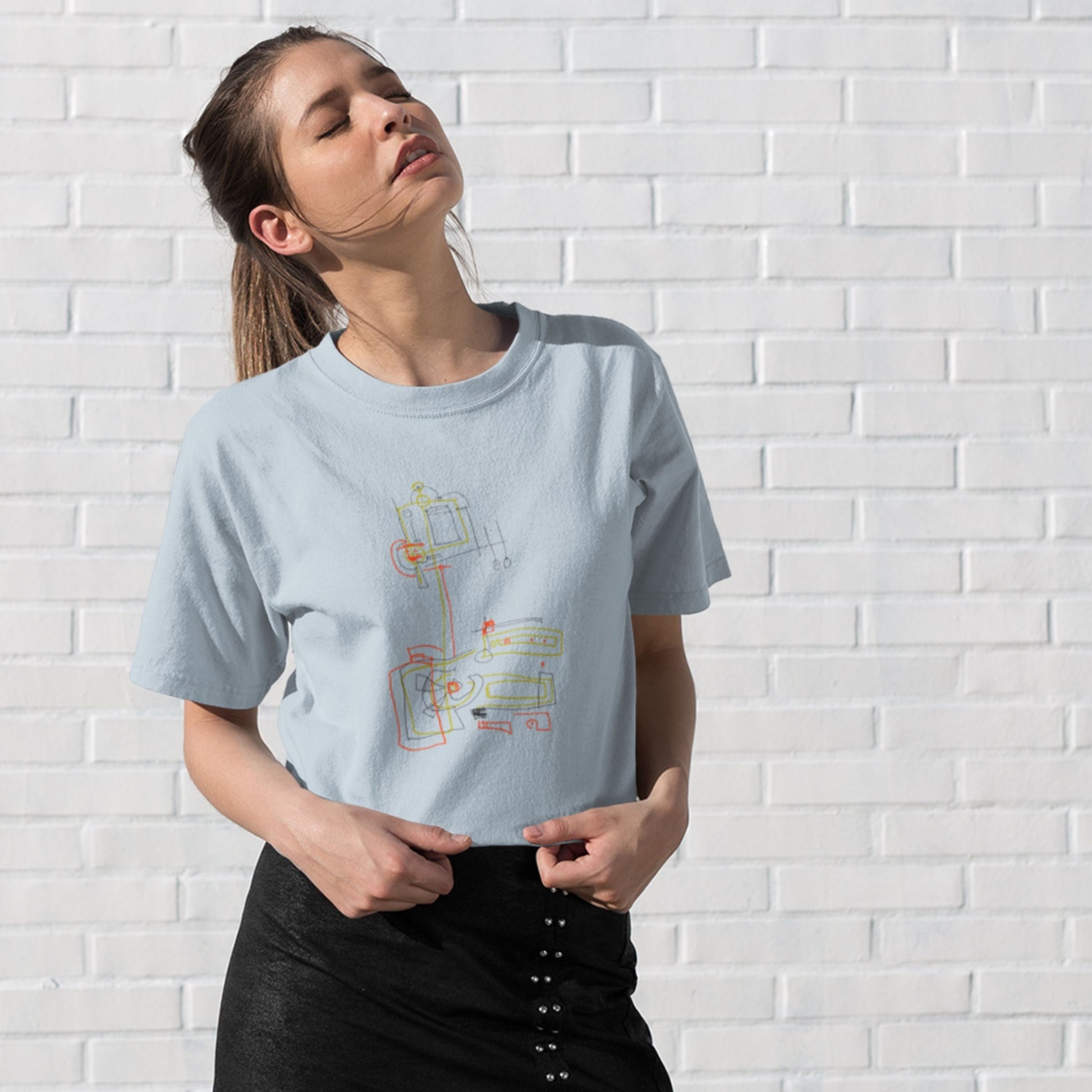 Woman wearing a light blue t-shirt with a colorful abstract drawing on a white brick background.