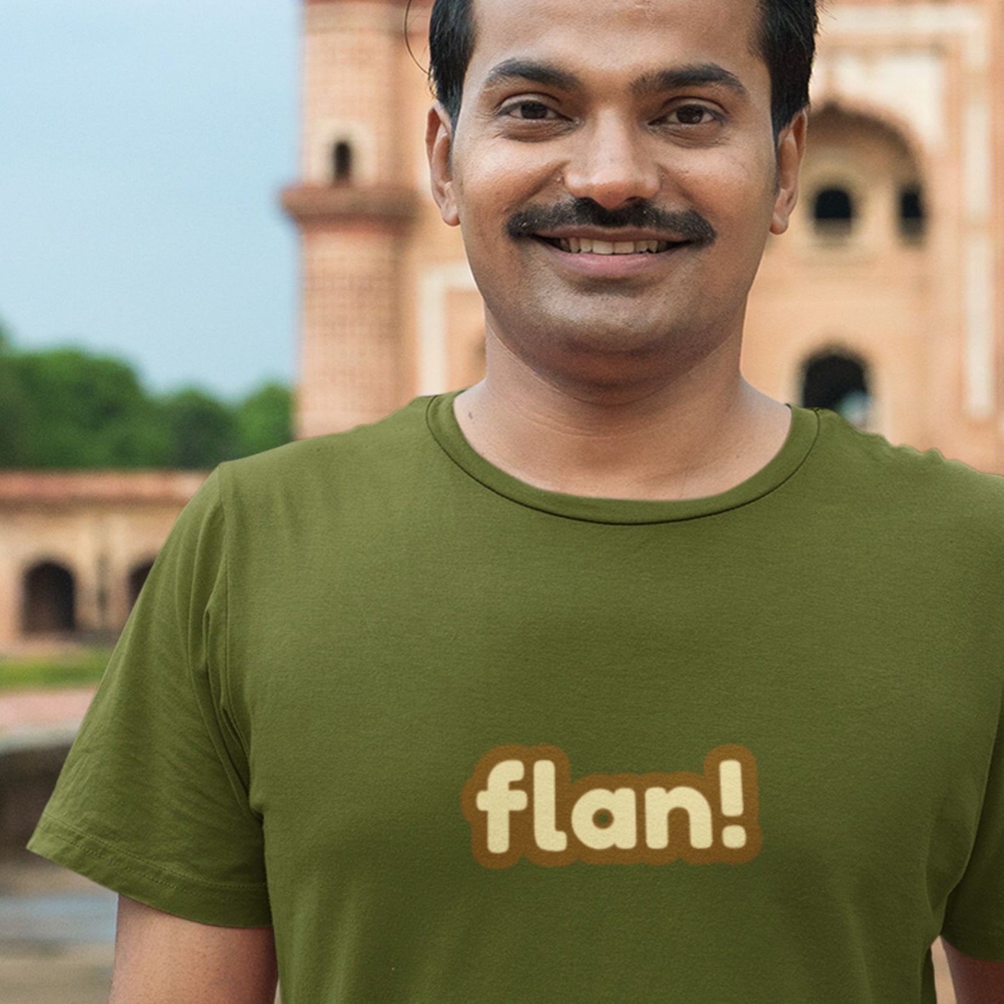 Man wearing a green t-shirt with 'flan!' text in front of an architectural background