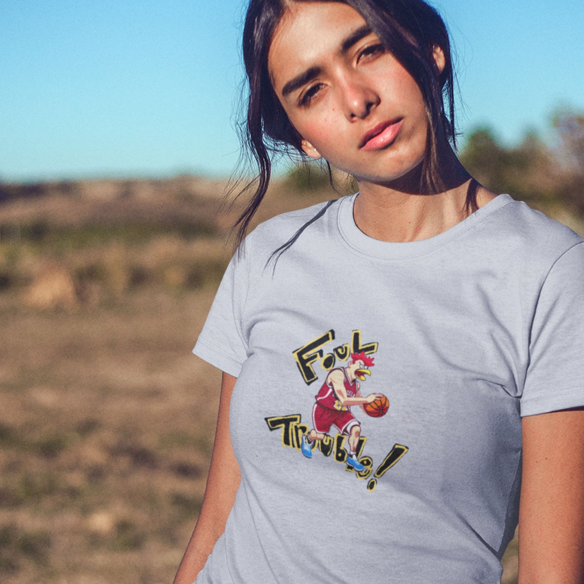 Curios woman wearing a light blue t-shirt with a fun, colorful basketball cartoon illustration in the desert.