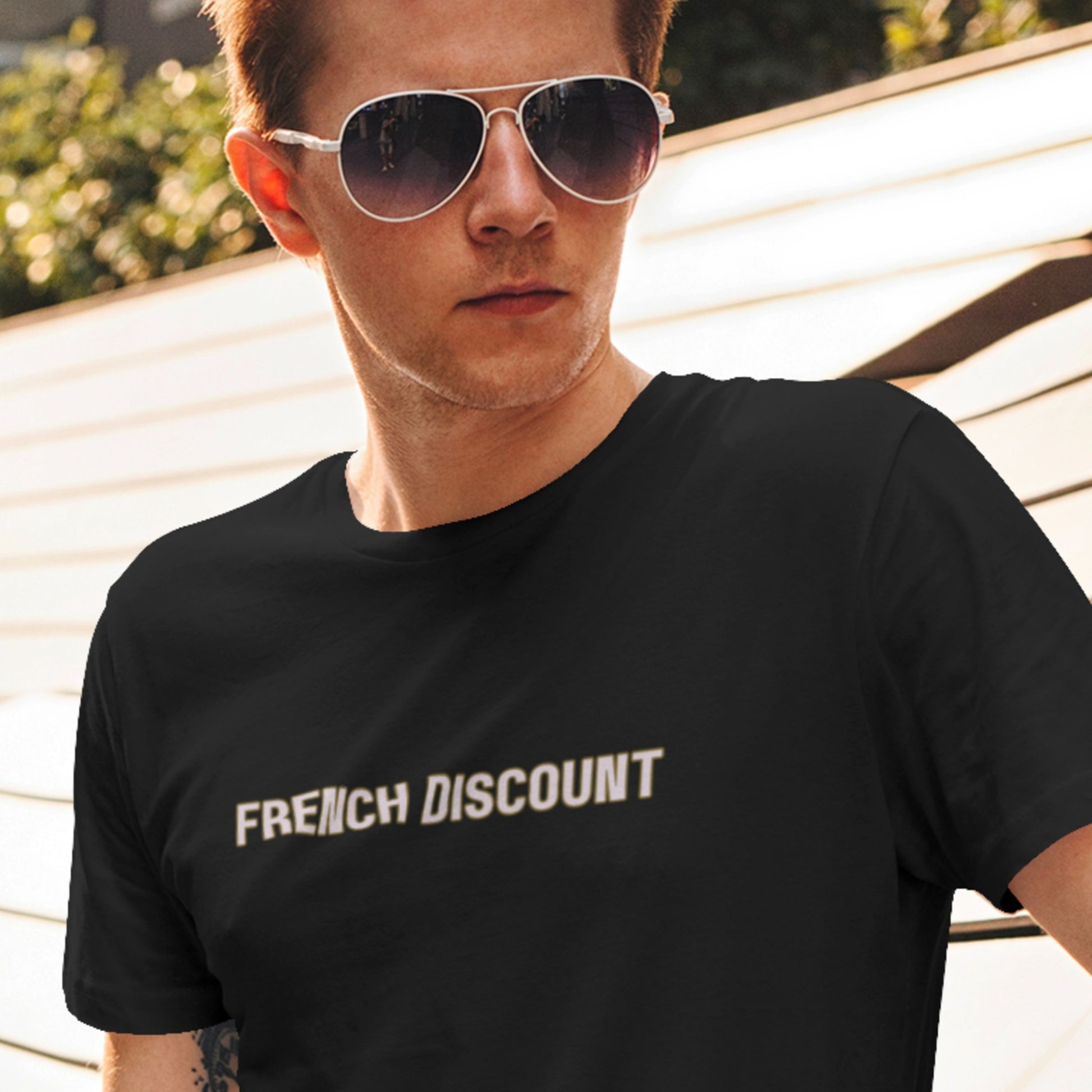 Cool guy wearing sunglasses and a black t-shirt with humorous colorful text in front of his house.