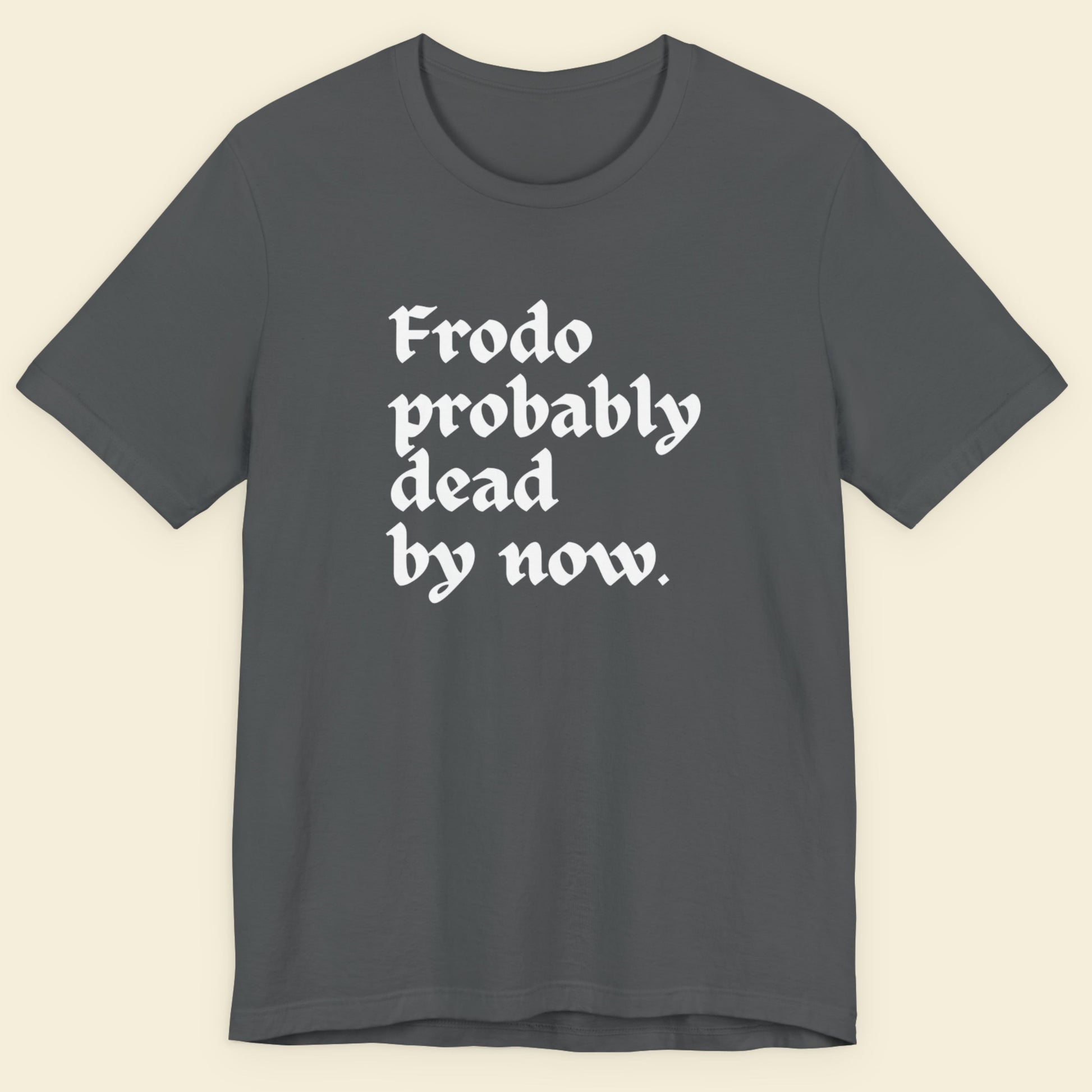 Gray t-shirt with white text 'Frodo probably dead by now' on a beige background.
