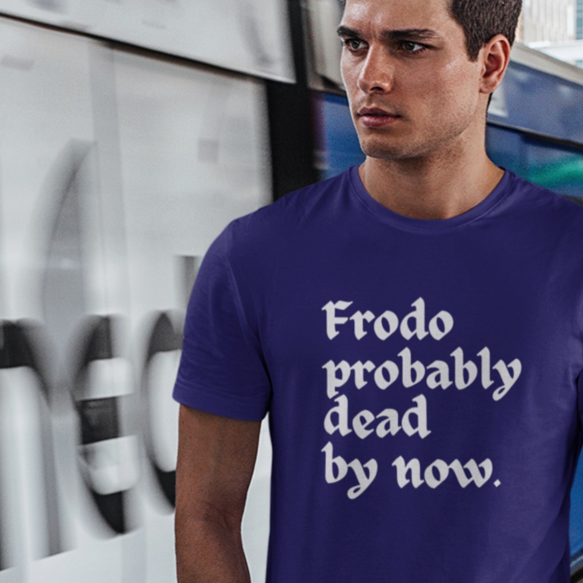 Man wearing a blue t-shirt with text standing in front of a modern architectural background.