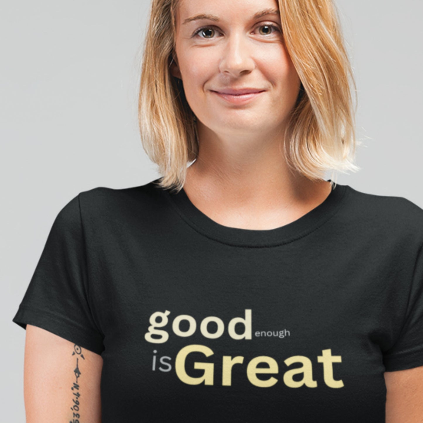 Person wearing a black t-shirt with 'good enough is Great' text on a plain background