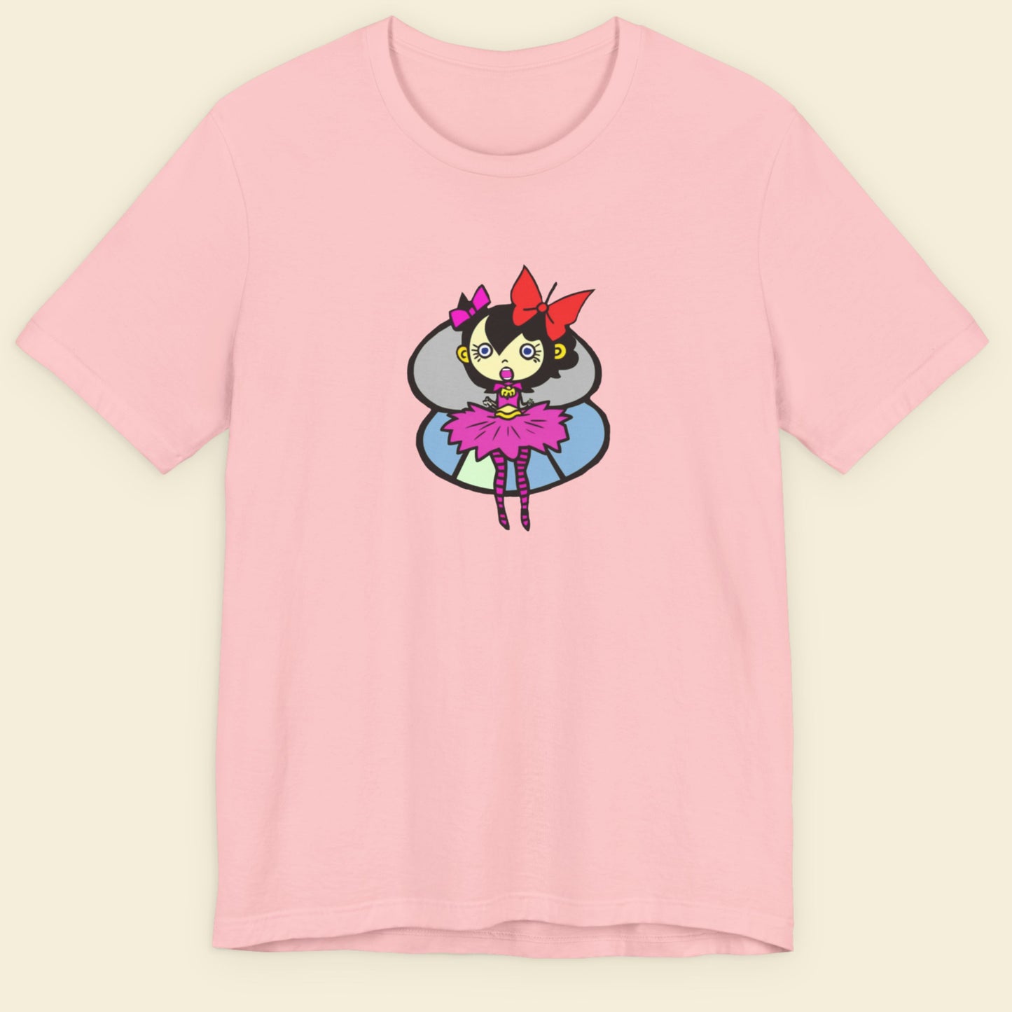Pink t-shirt with a fun, colorful cartoon pixie illustration on a beige background.