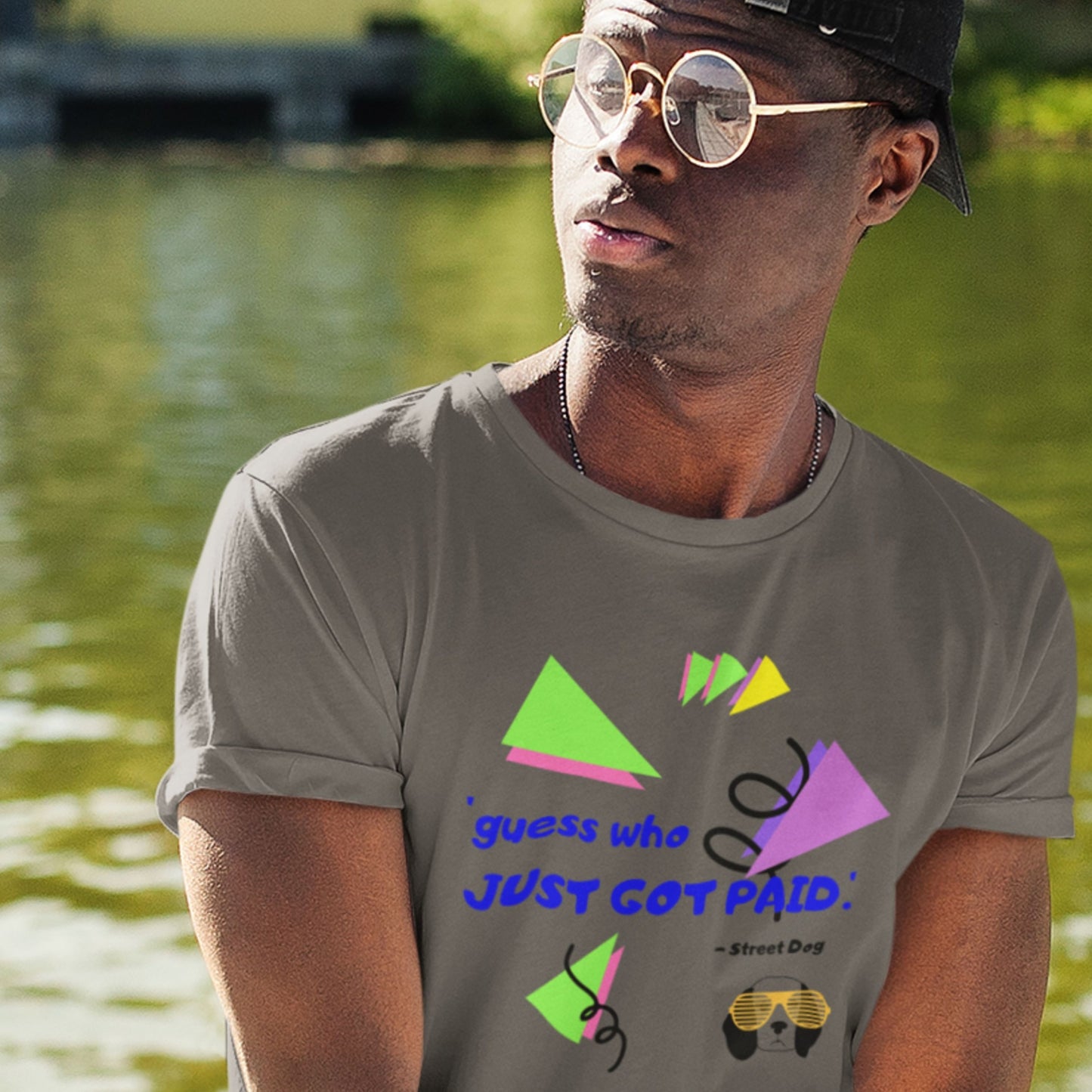 Man wearing a gray t-shirt with colorful graphics and text by a body of water.