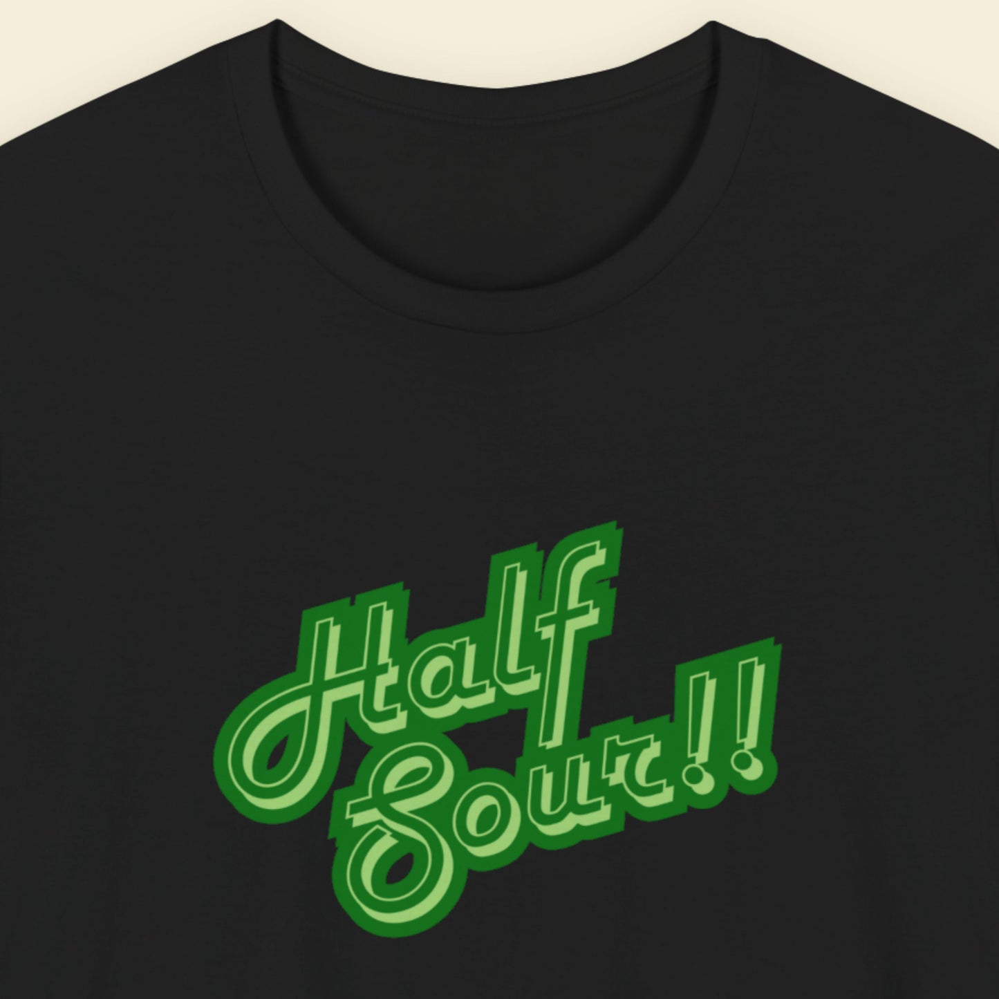 Black shirt with green 'half sour!!' text on a beige background.