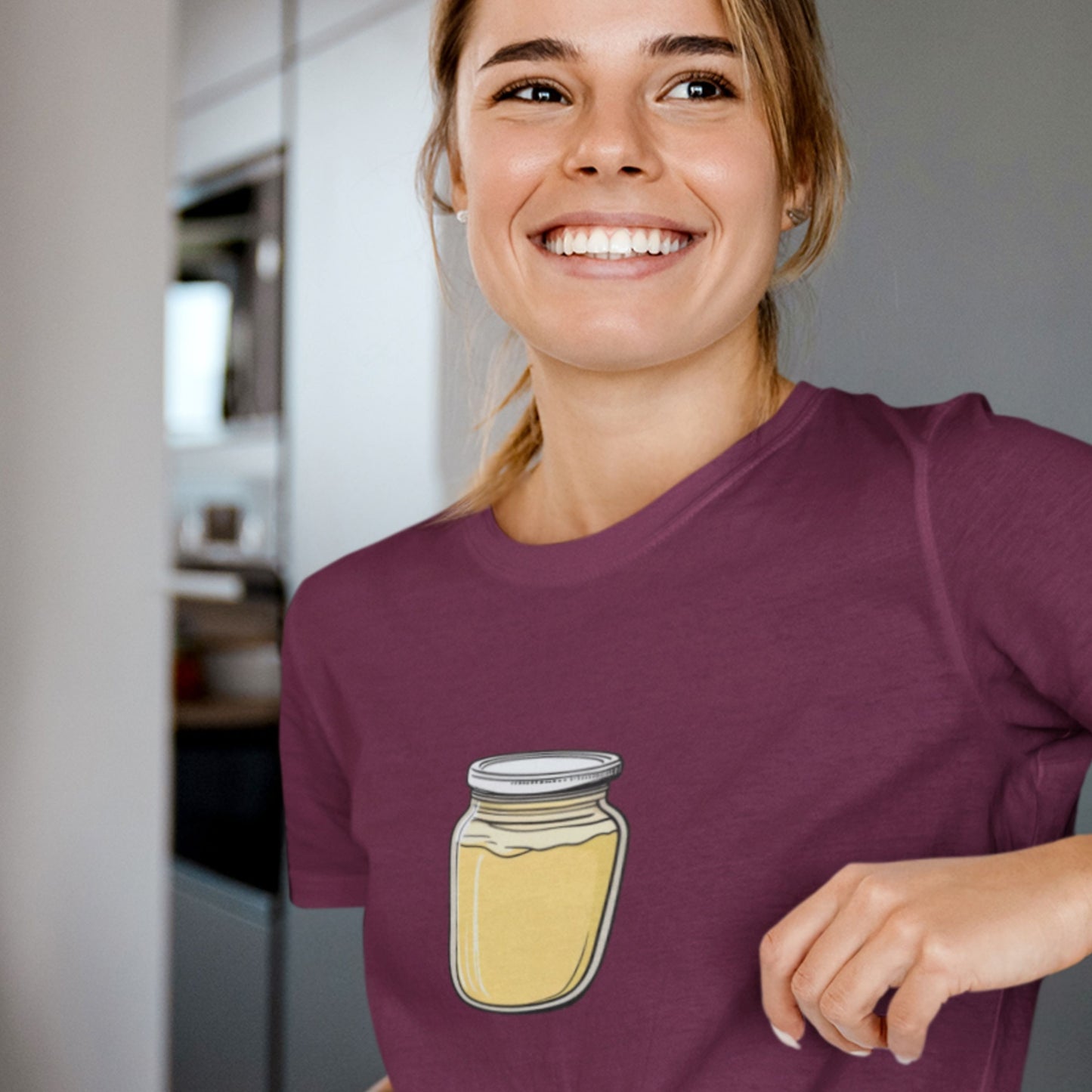 Woman smiling and wearing a maroon t-shirt with a drawing of a jar of Dijon mustard.