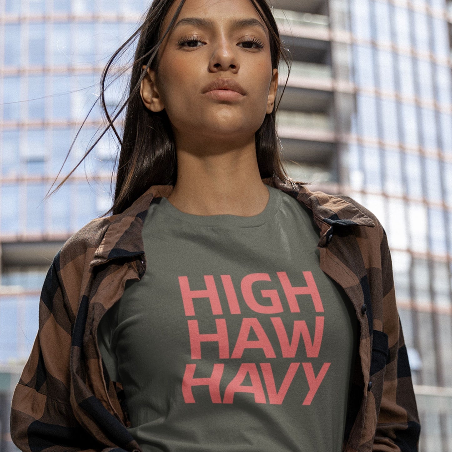 Confidant woman wearing an army green t-shirt with multicolored nonsensical  'high haw havy' text in the city.