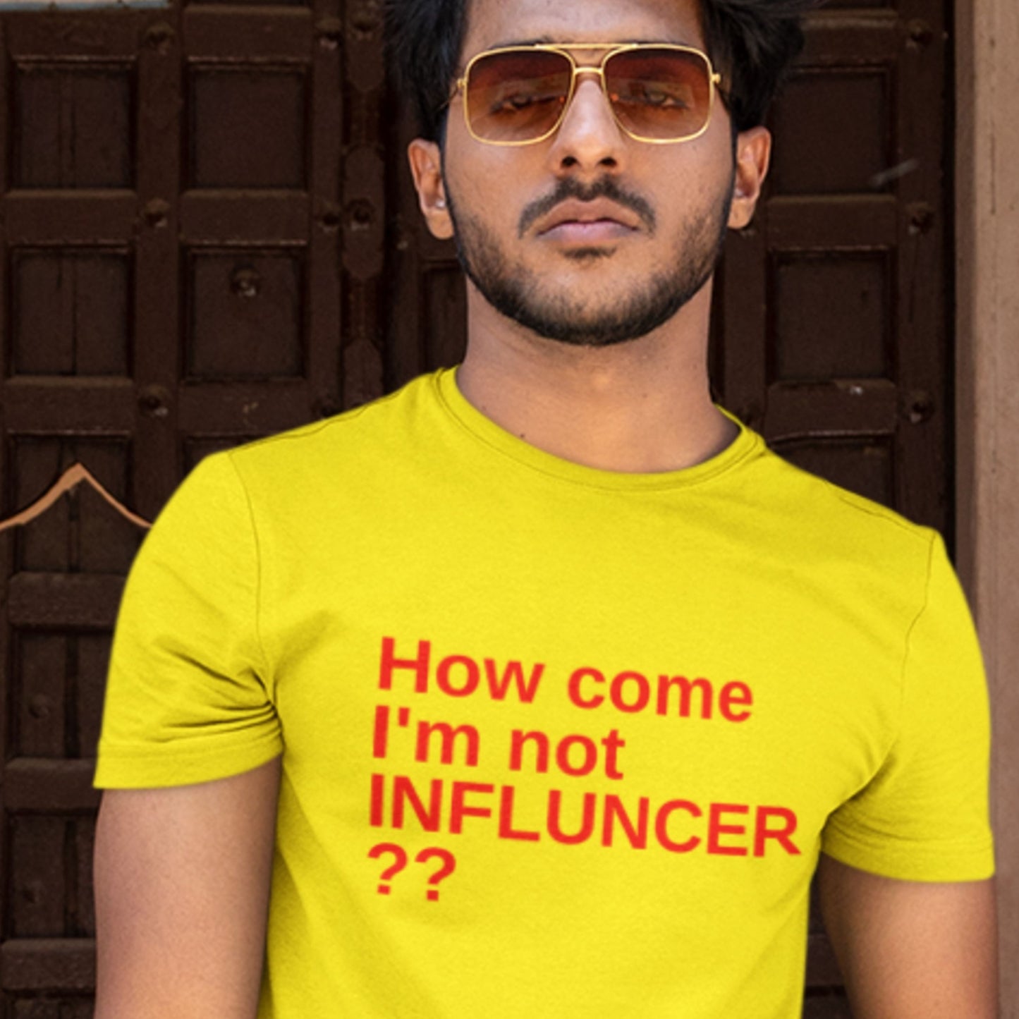 Man wearing a yellow t-shirt with red text in front of a brown door.
