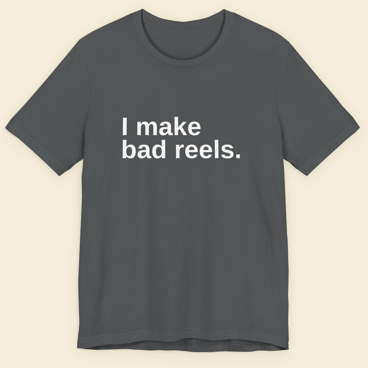 Gray t-shirt with 'I make bad reels' text on a beige background.