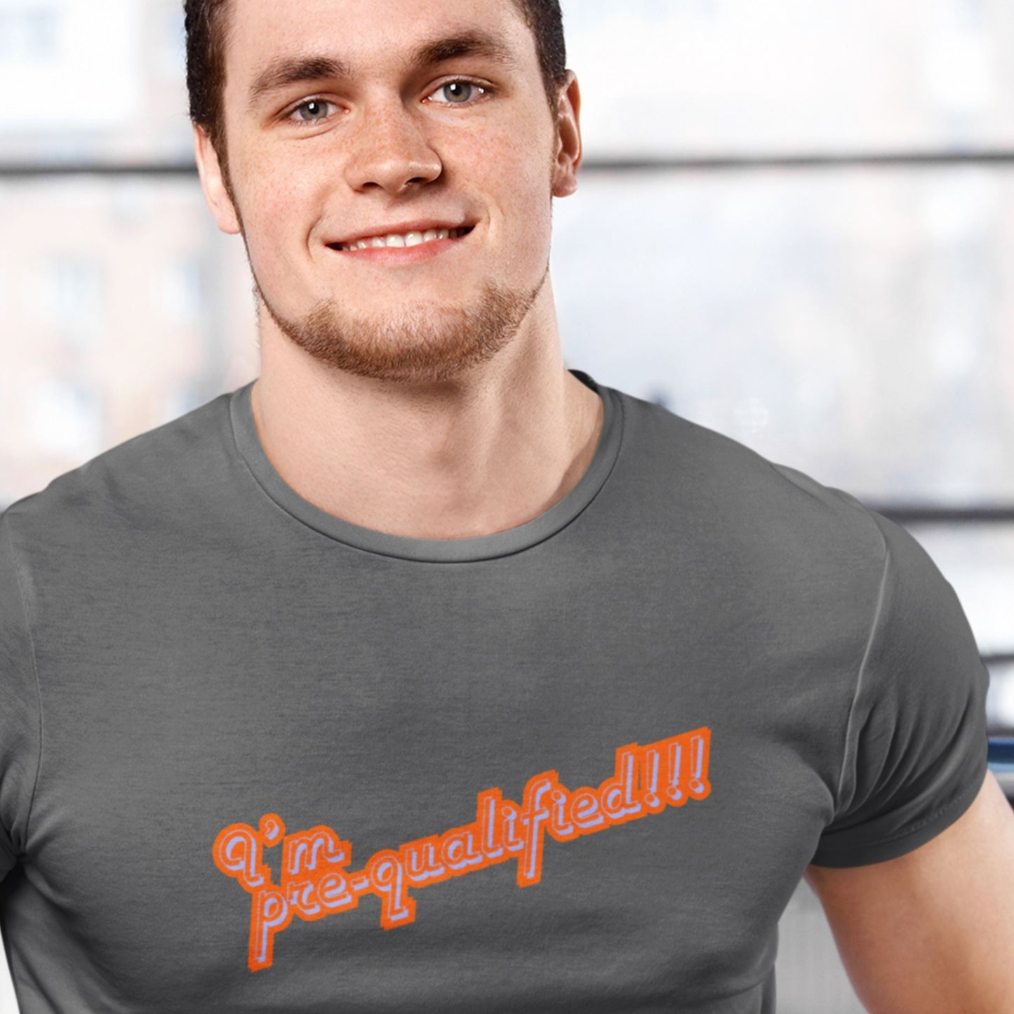 Smiling man wearing a grey t-shirt with multicolored text reading 'I'm pre-qualified!!!' on a grey background.