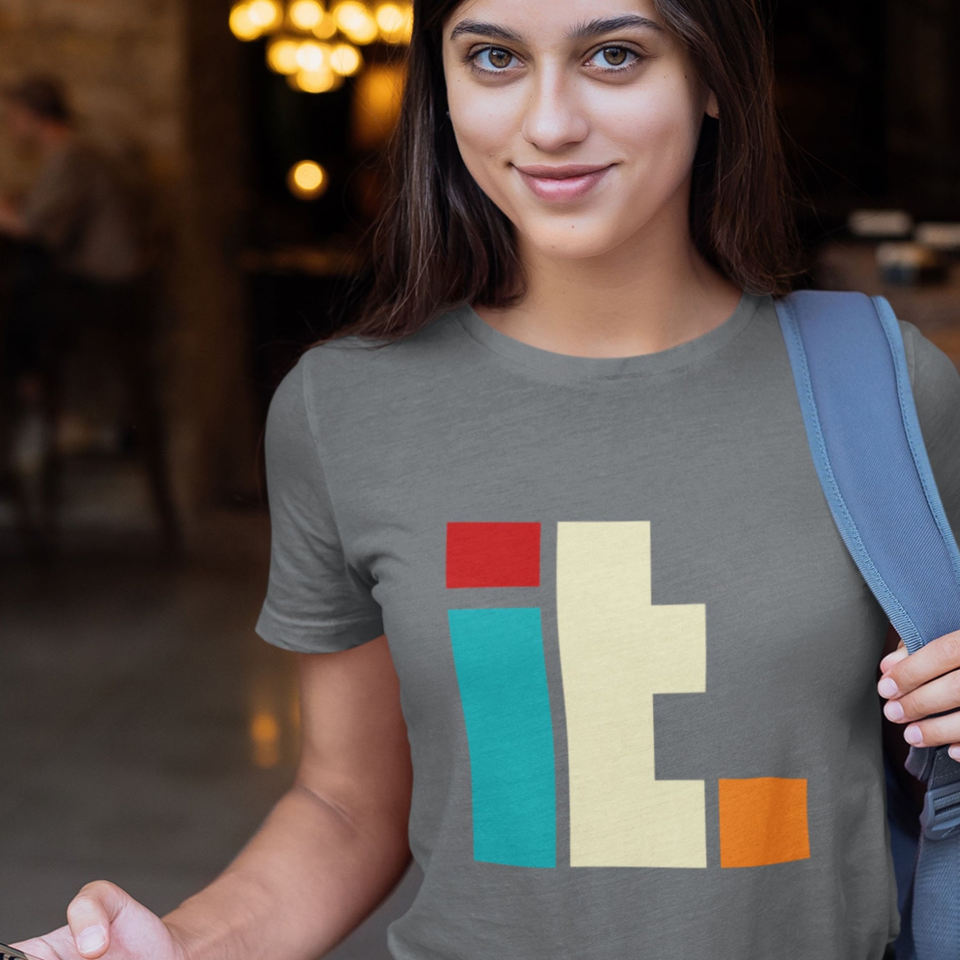 Woman wearing a gray t-shirt with colorful geometric design in an indoor setting.