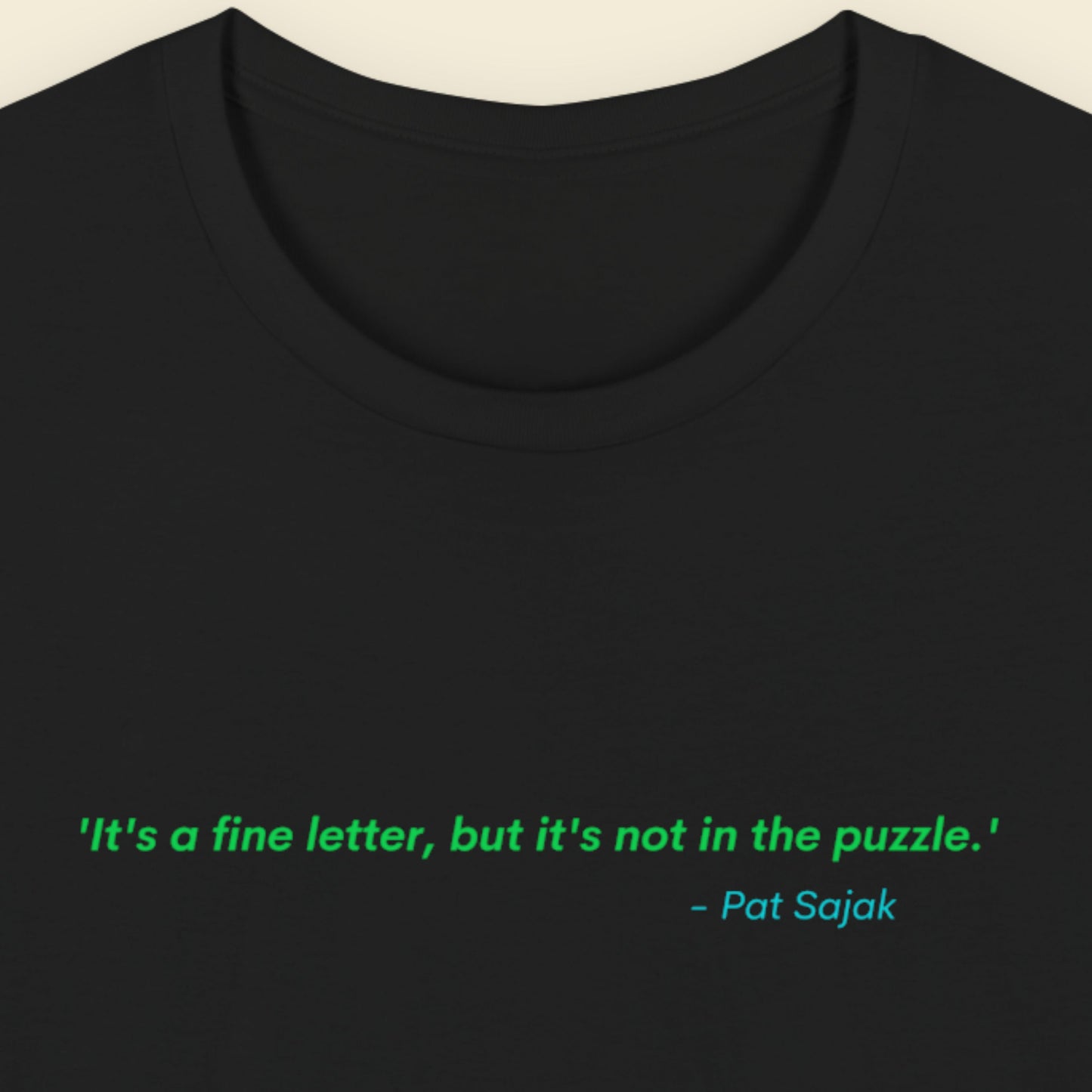 Black t-shirt with green text quote by Pat Sajak on a beige background.