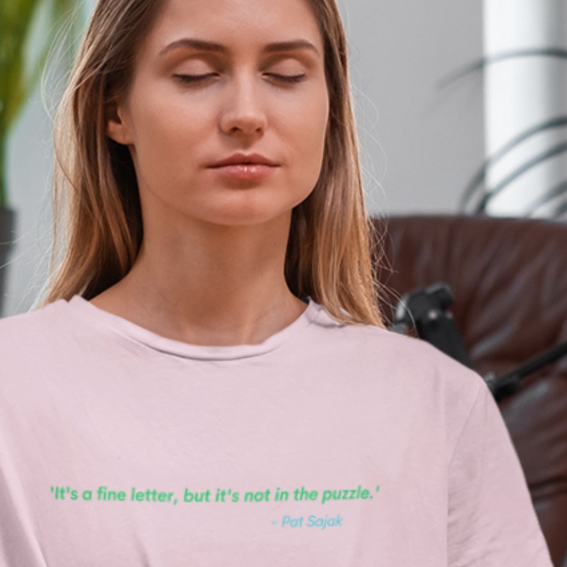 Woman wearing a pink shirt with a quote, sitting in a blurred indoor setting.