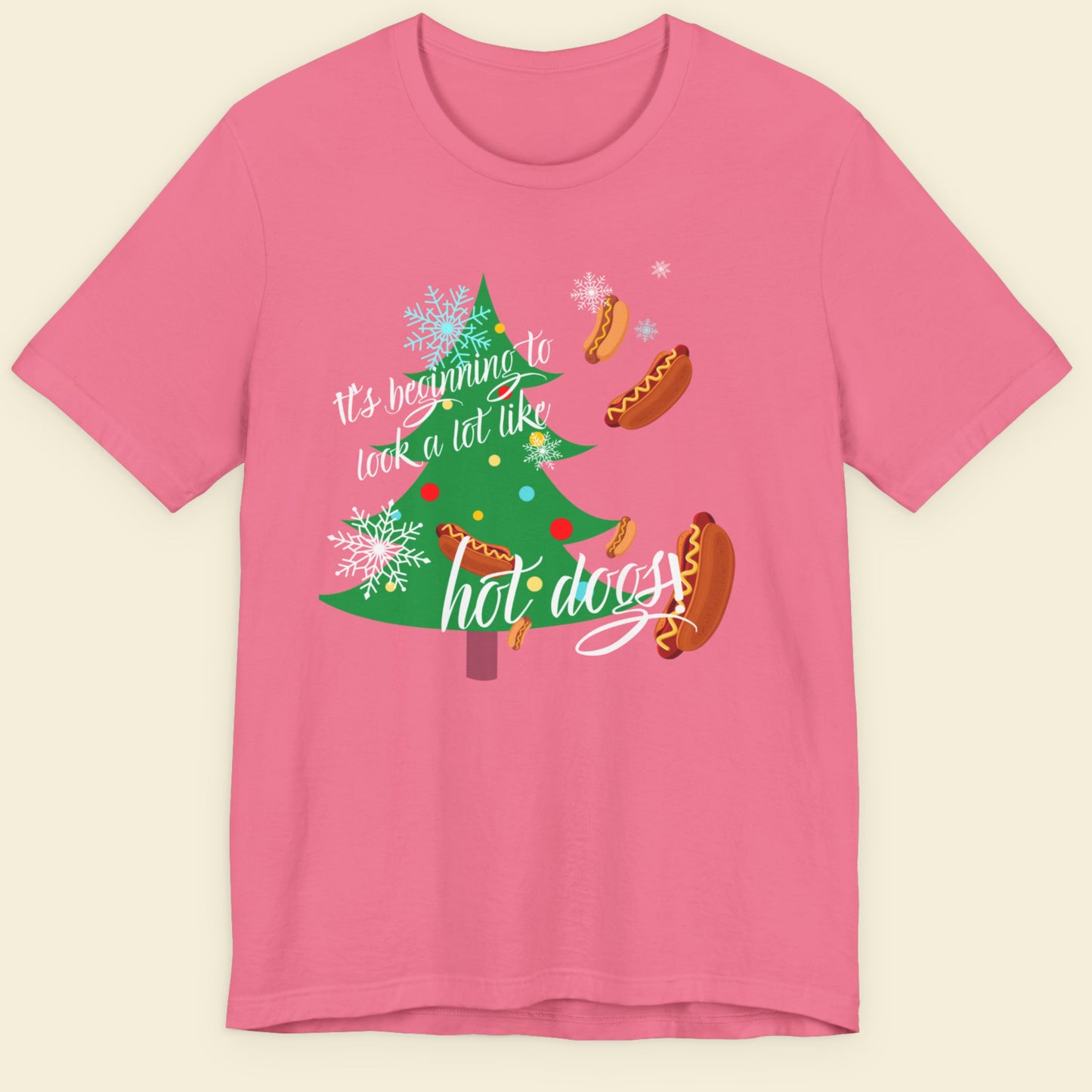Pink t-shirt with Christmas-themed design featuring a tree and hot dogs on a beige background.