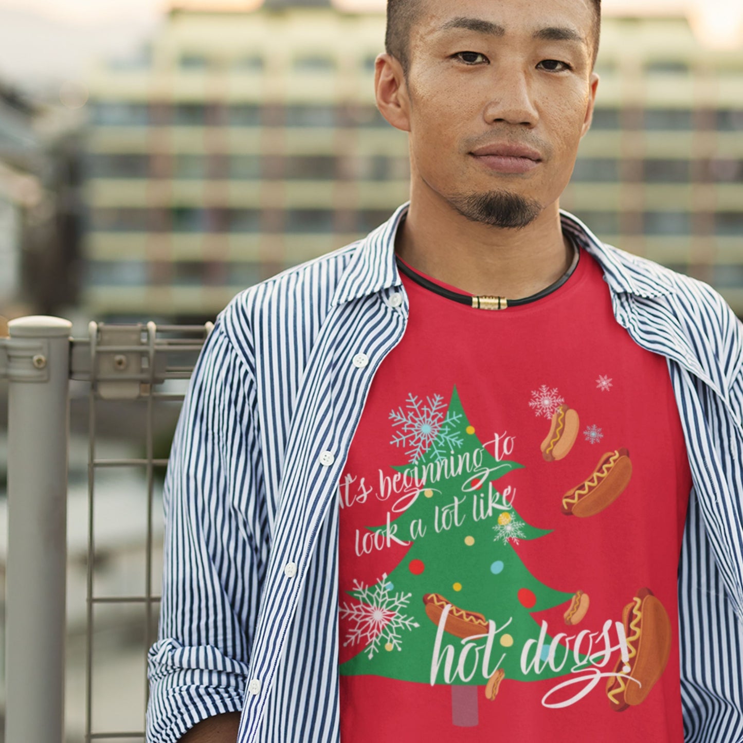 Man wearing a red t-shirt with a Christmas tree and hot dog design, standing outdoors..