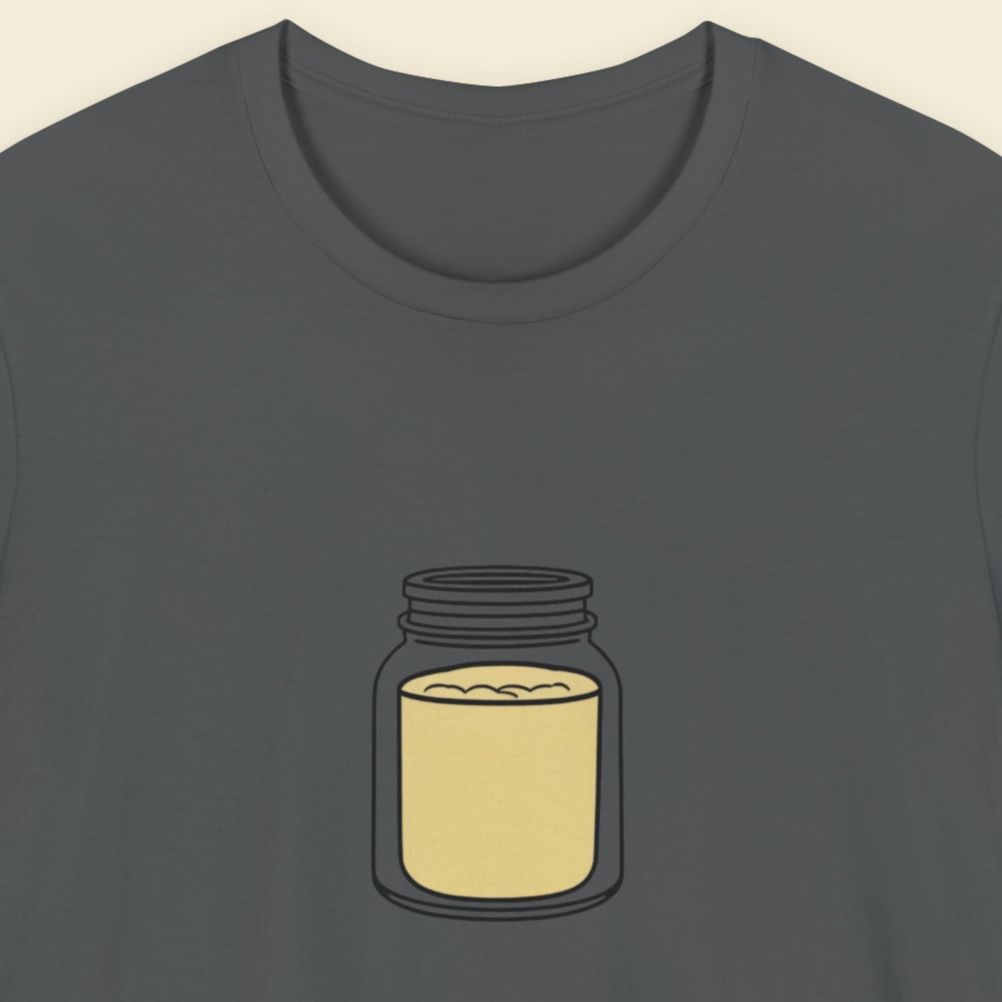 Grey t-shirt with a drawing of a jar of mustard powder on a beige background.