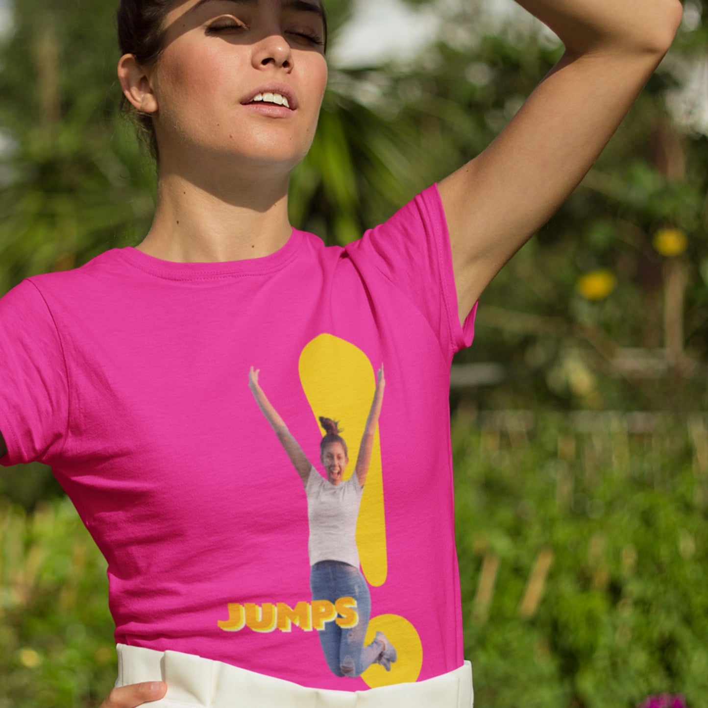 Woman wearing a pink t-shirt with a graphic of a person jumping and the word 'JUMPS' outdoors.