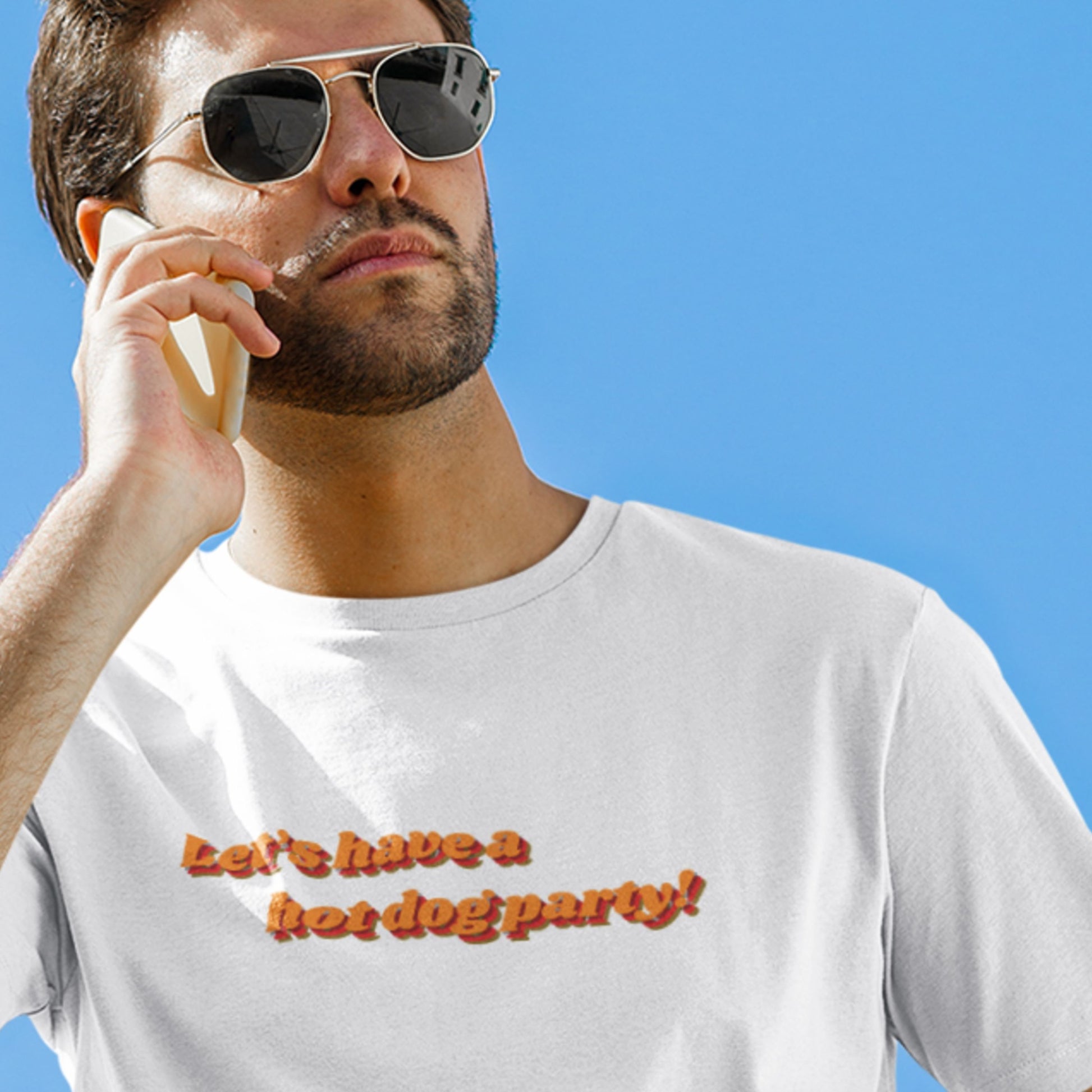Man wearing sunglasses and a white t-shirt with text against a blue sky