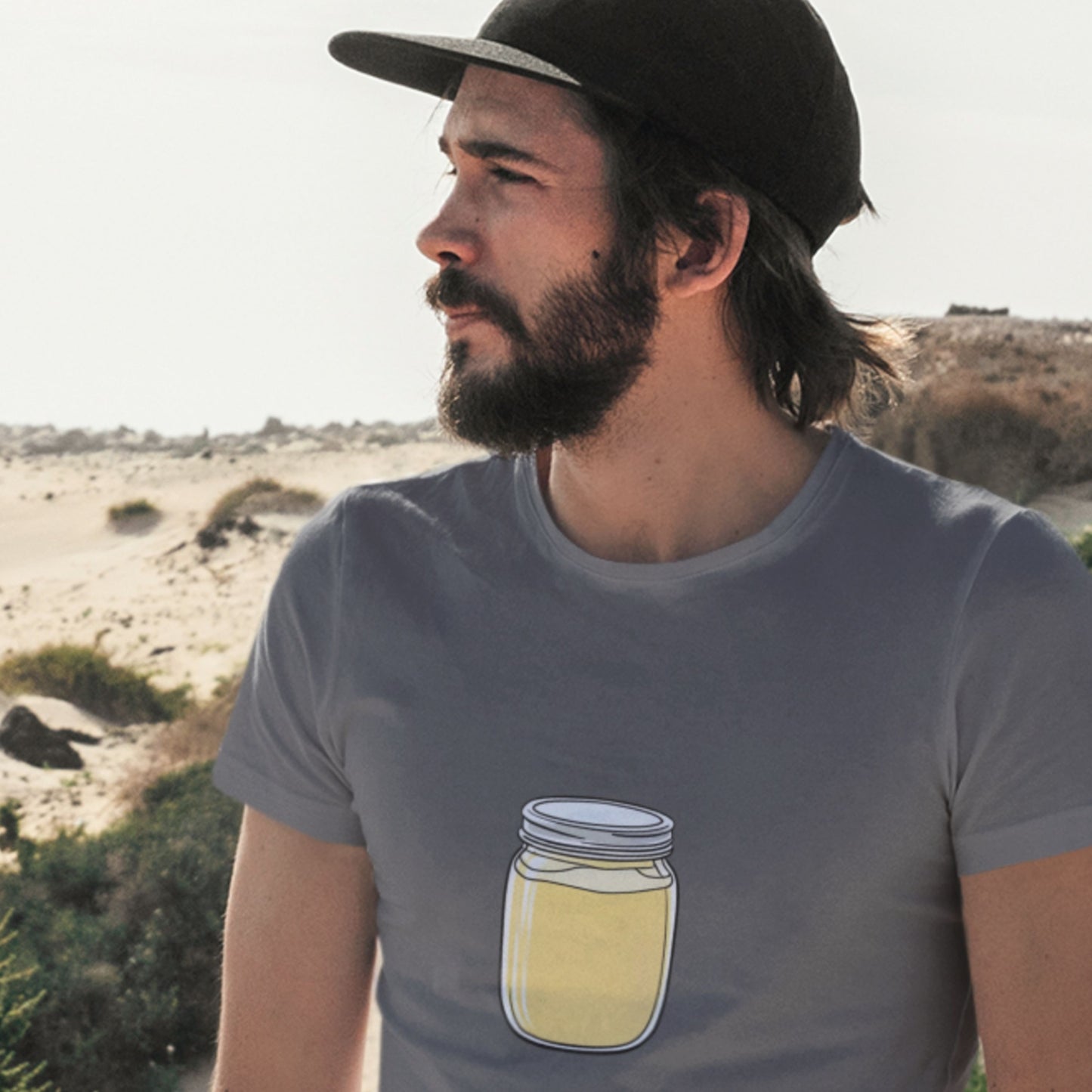 Man wearing a grey t-shirt with a fun, colorful cartoon illustration on a beach.