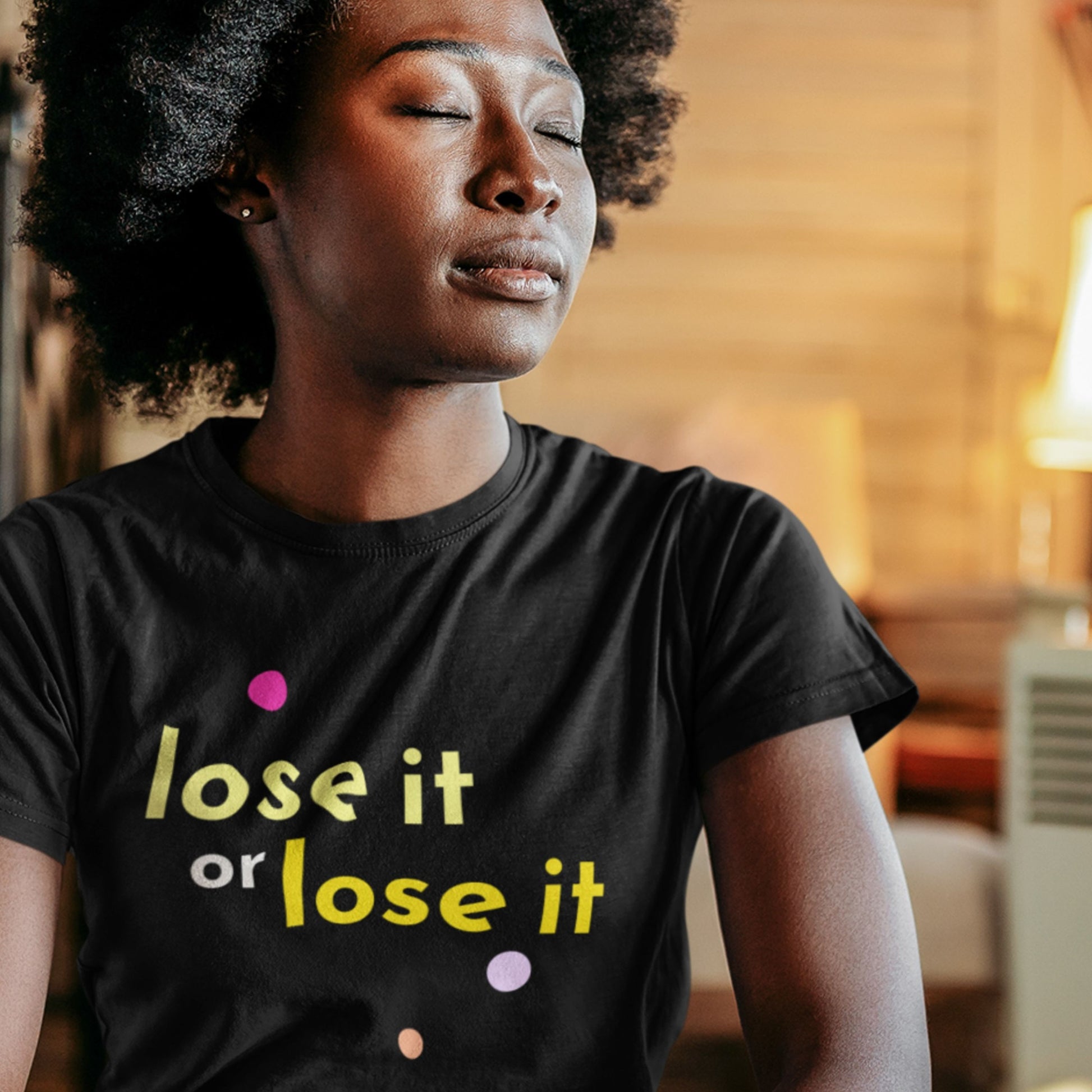 Person wearing a black t-shirt with 'lose it or lose it' text in a warm indoor setting.
