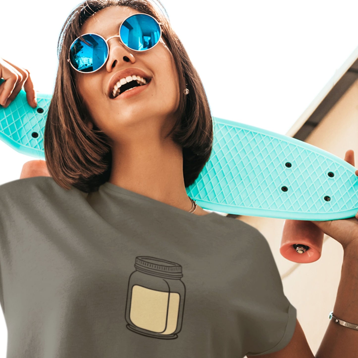 Person holding a turquoise skateboard with a gray t-shirt featuring a jar design.