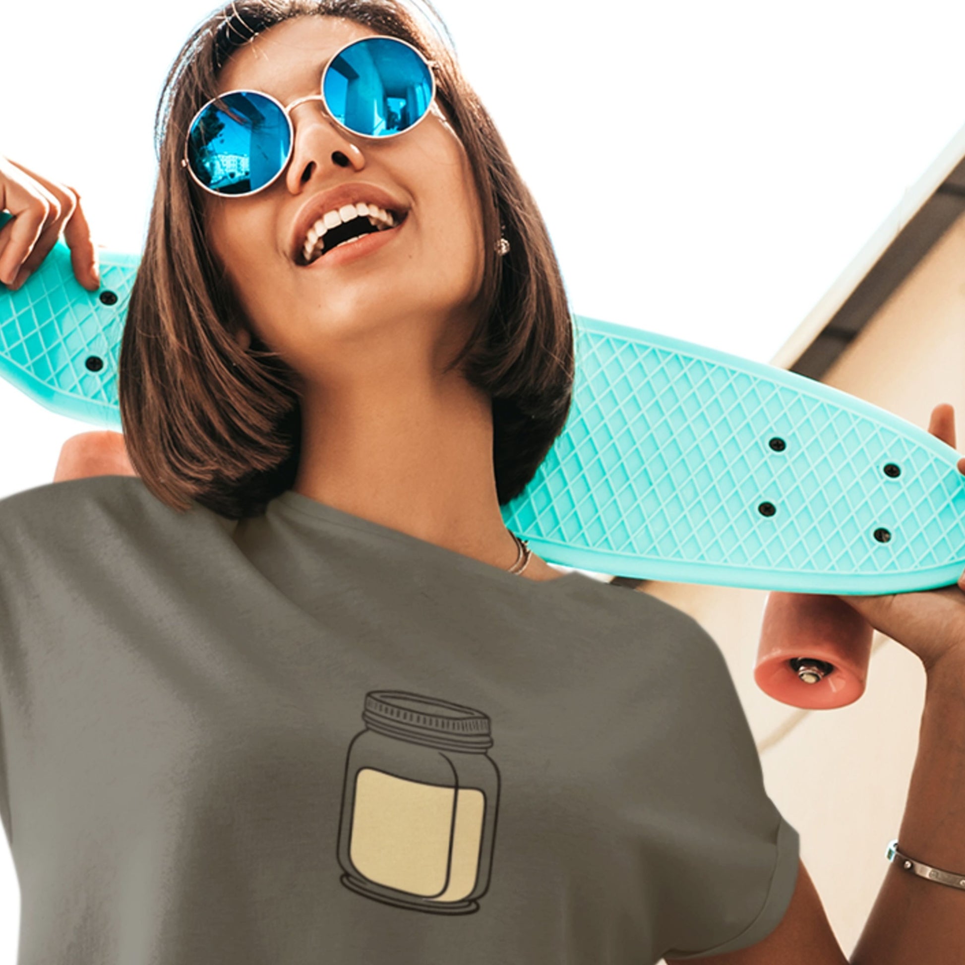 Person holding a turquoise skateboard with a gray t-shirt featuring a jar design.