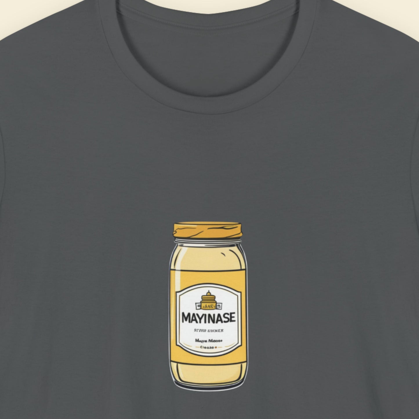 Grey t-shirt with a drawing of a jar of Mayinase on a beige background.