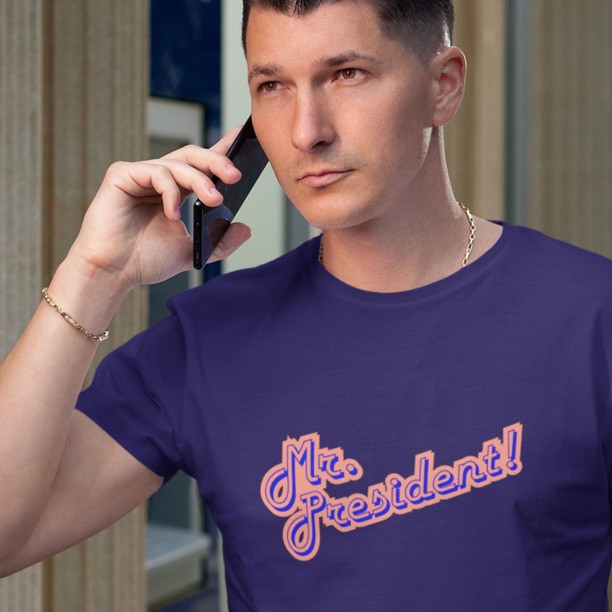 Man wearing a navy t-shirt with 'Mr. President!' text in orange and blue on the phone.