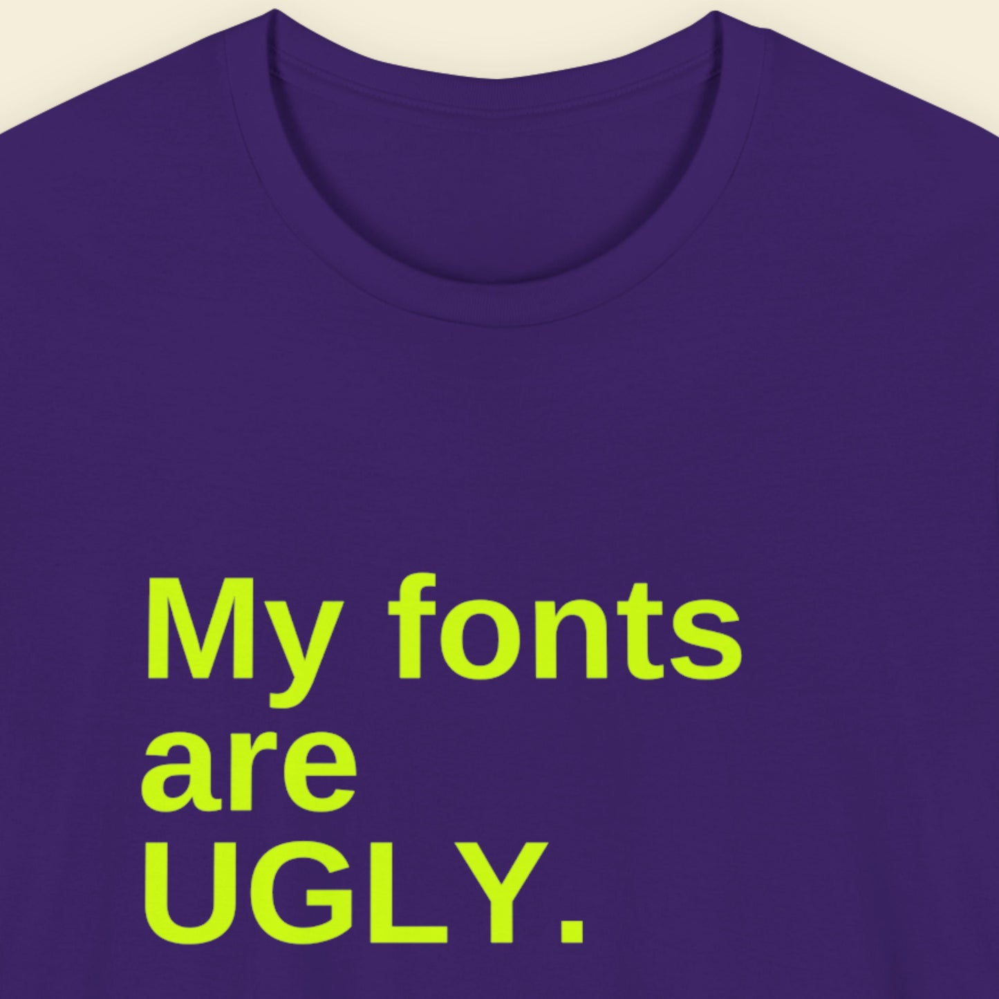 Purple t-shirt with humorous colorful text on a beige background.