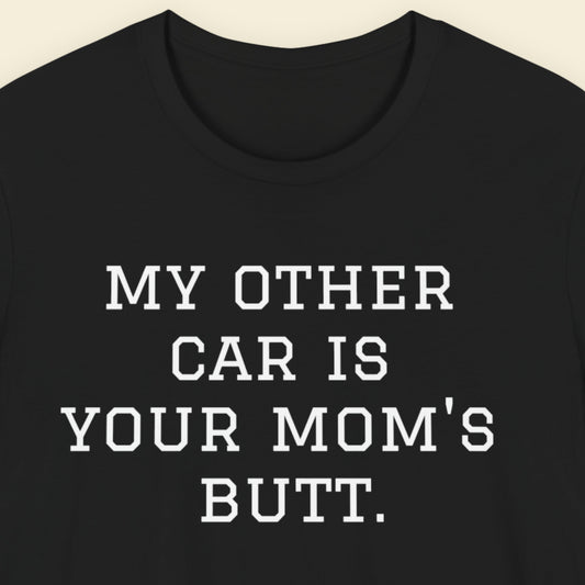 Black t-shirt with white text 'MY OTHER CAR IS YOUR MOM'S BUTT.' on a beige background.