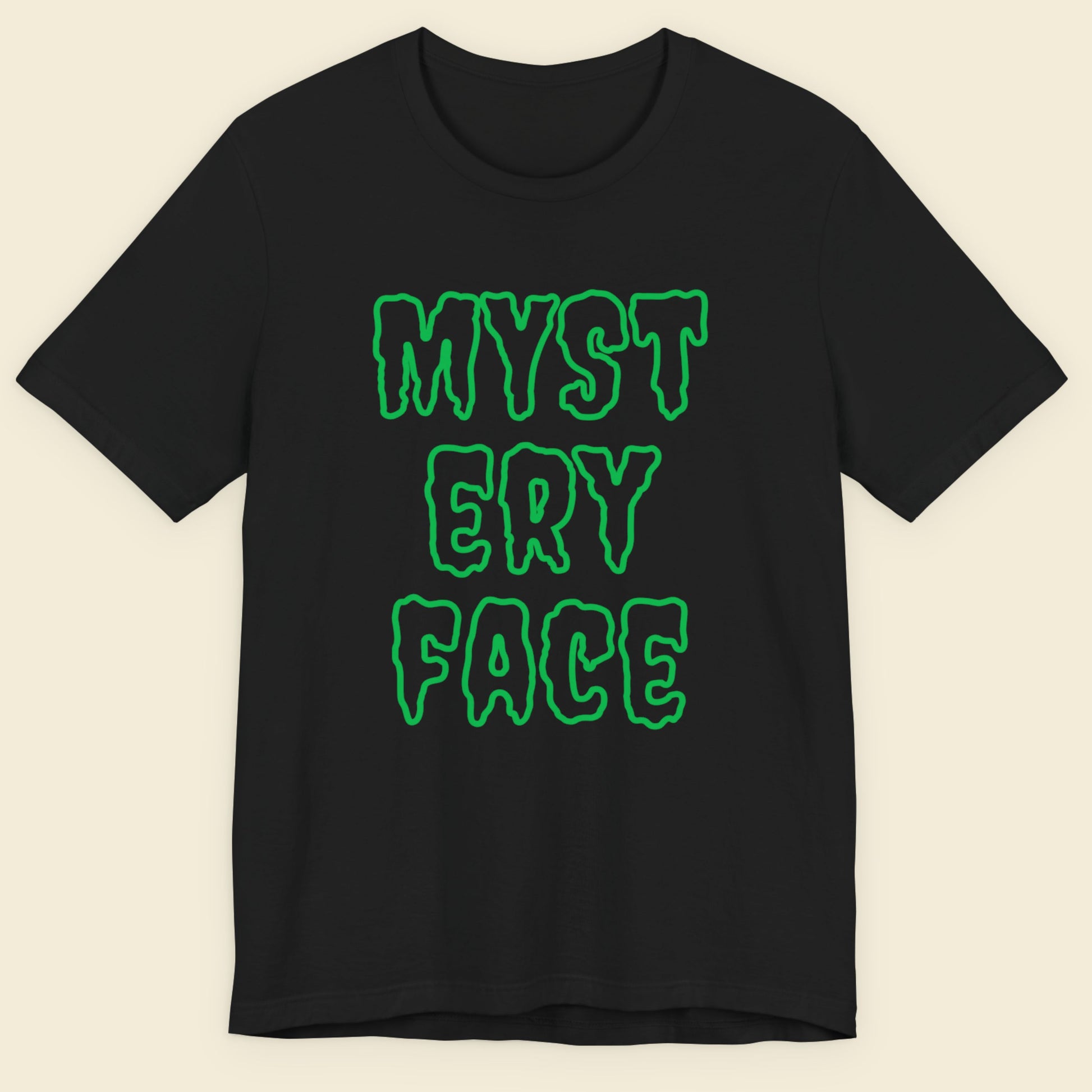 Black t-shirt with green text 'MYSTERY FACE' on a beige background.