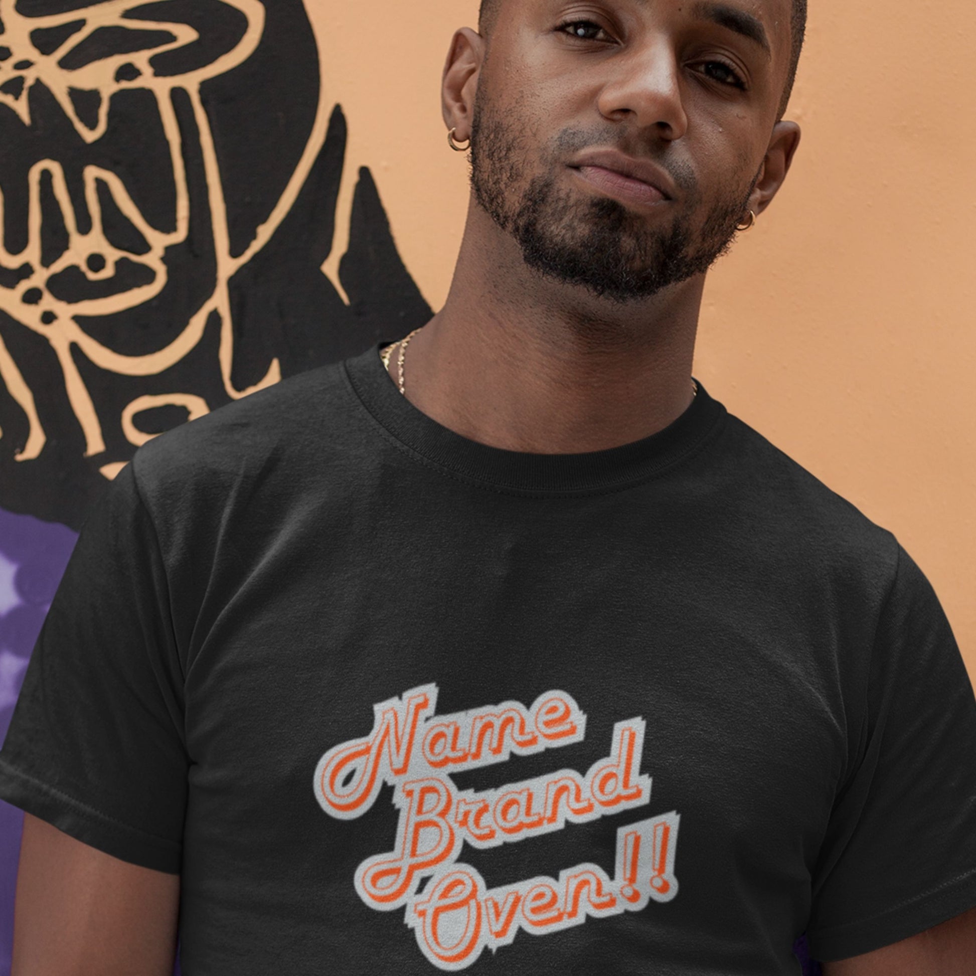 Man wearing a black t-shirt with 'Name Brand Over!' text against a colorful background.
