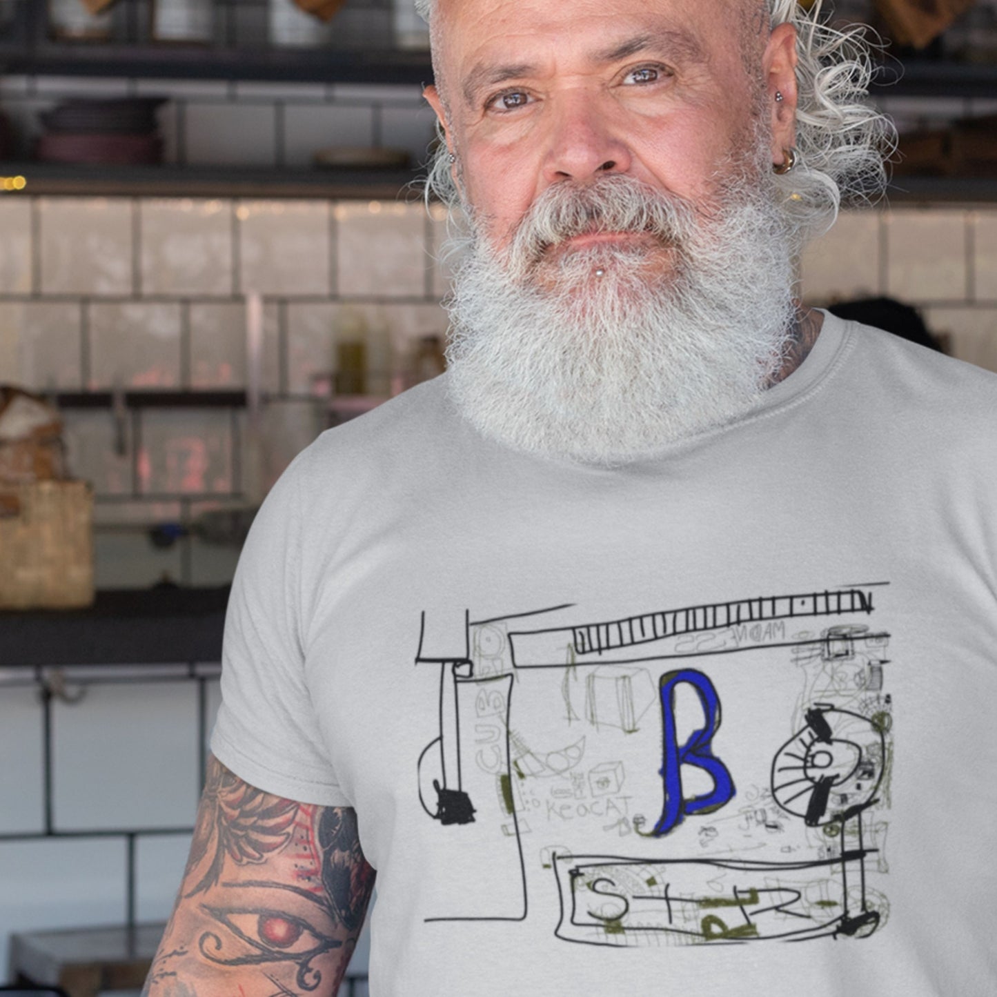 Man with a white beard wearing a gray t-shirt with a graphic design in a kitchen setting.