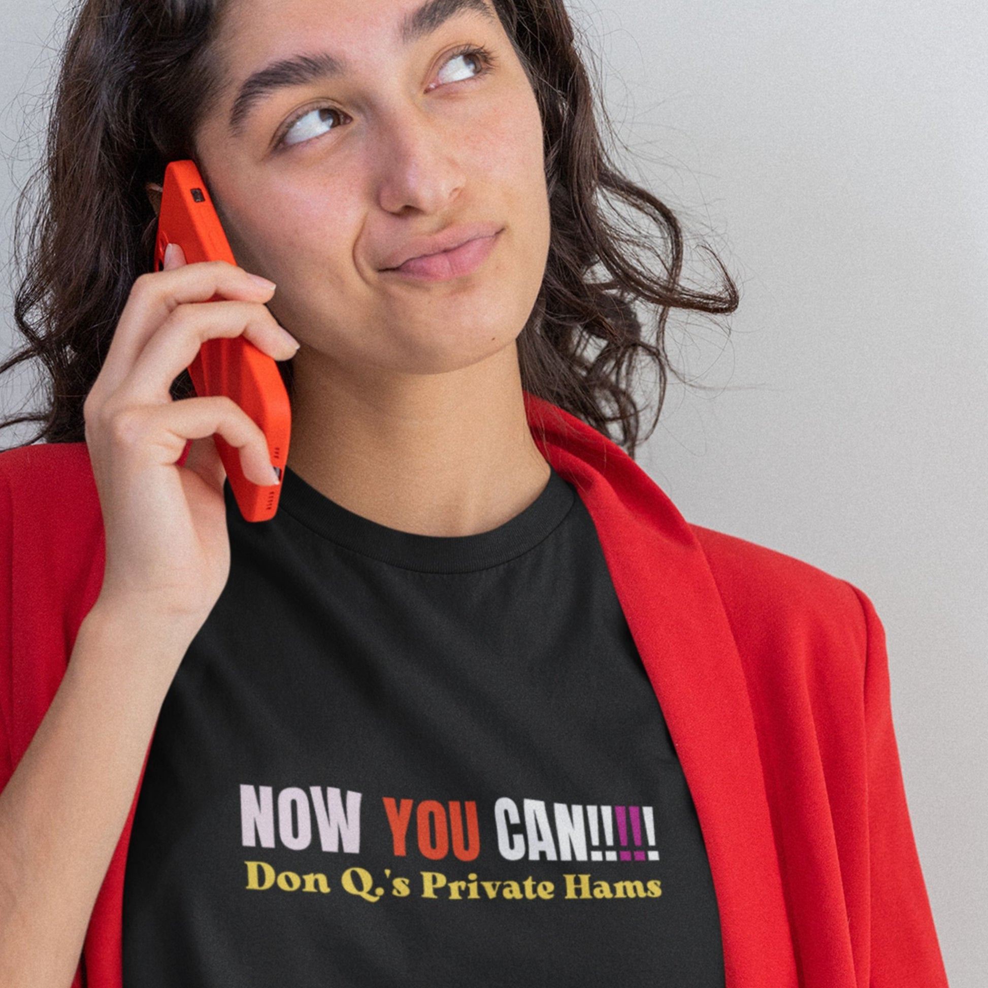 Person wearing a black t-shirt with colorful text, holding an orange phone.