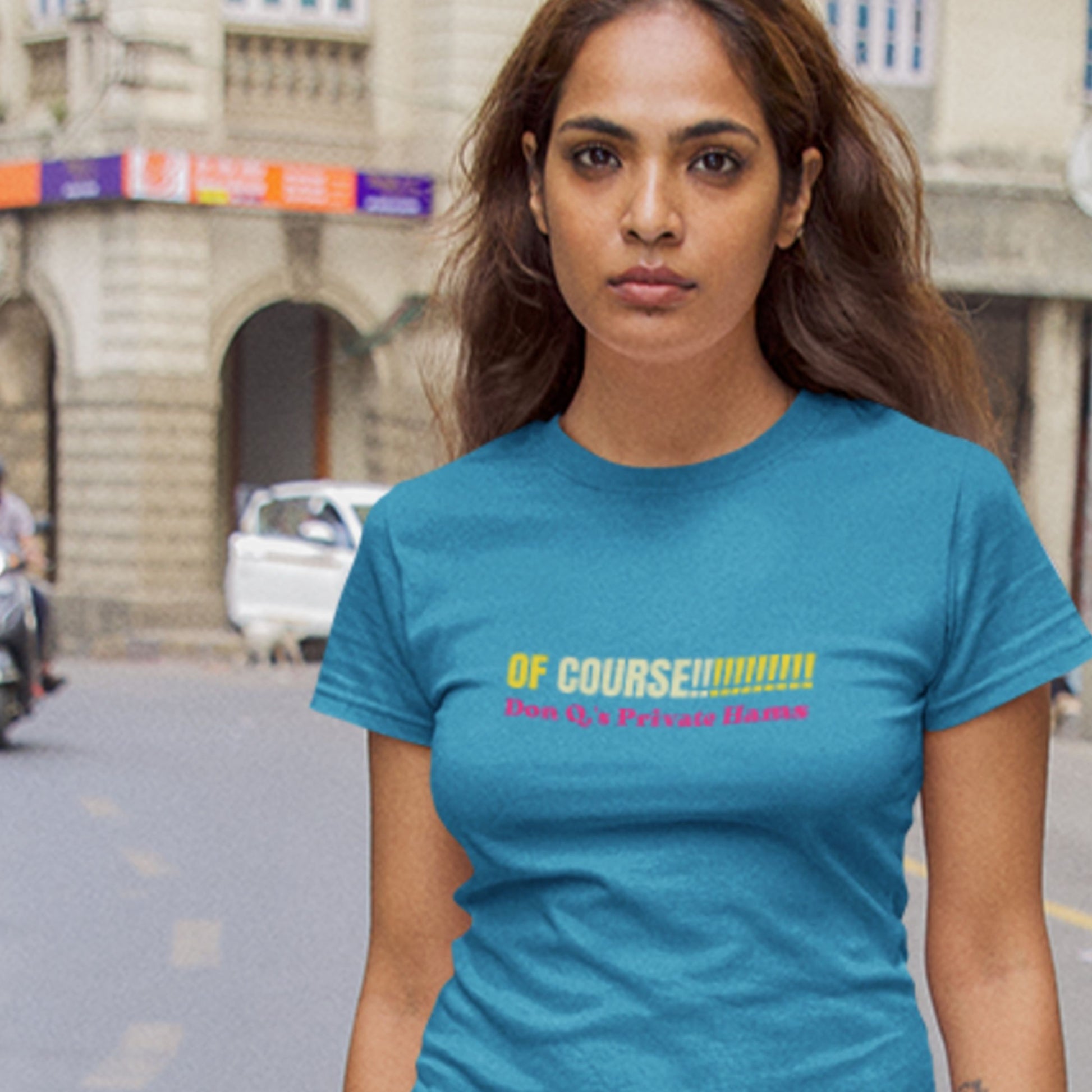 Woman in Europe wearing an aqua blue tee with multicolored 'of course!!!!!!!!!!!' text on the street.