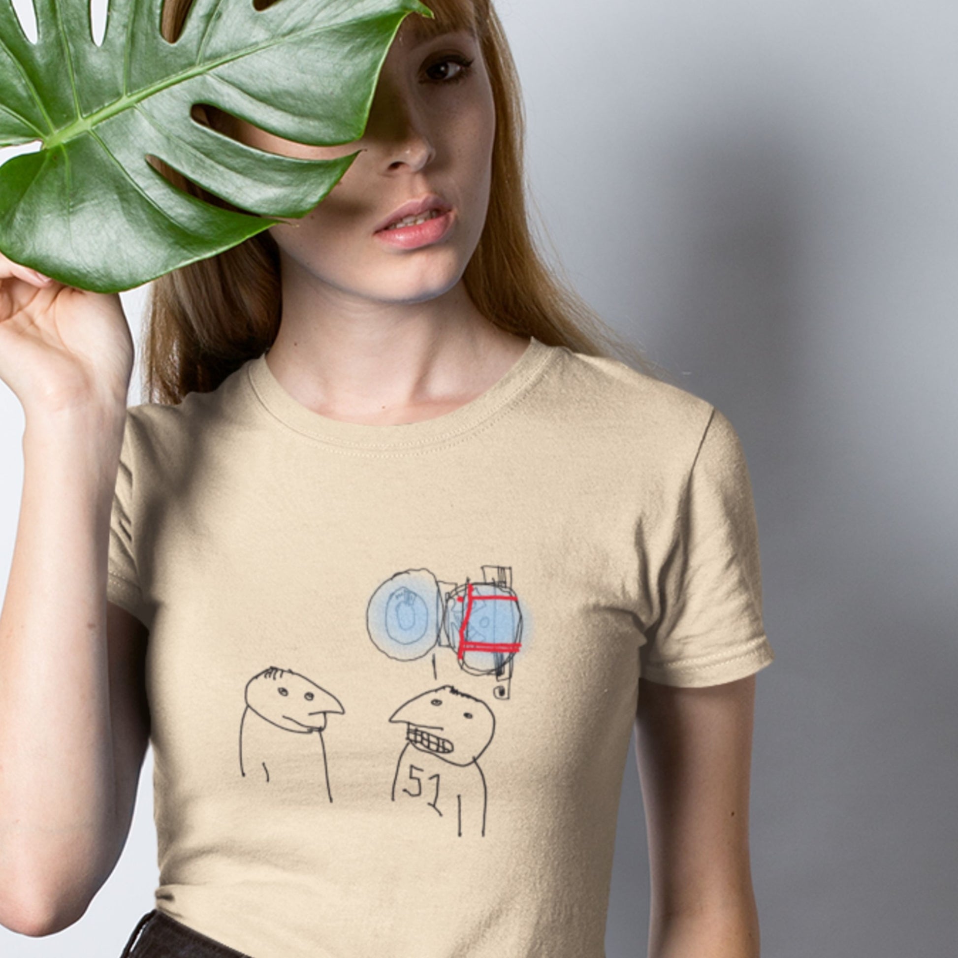 Woman, hiding behind a plant and wearing a beige t-shirt with a colorful abstract drawing on a grey background.