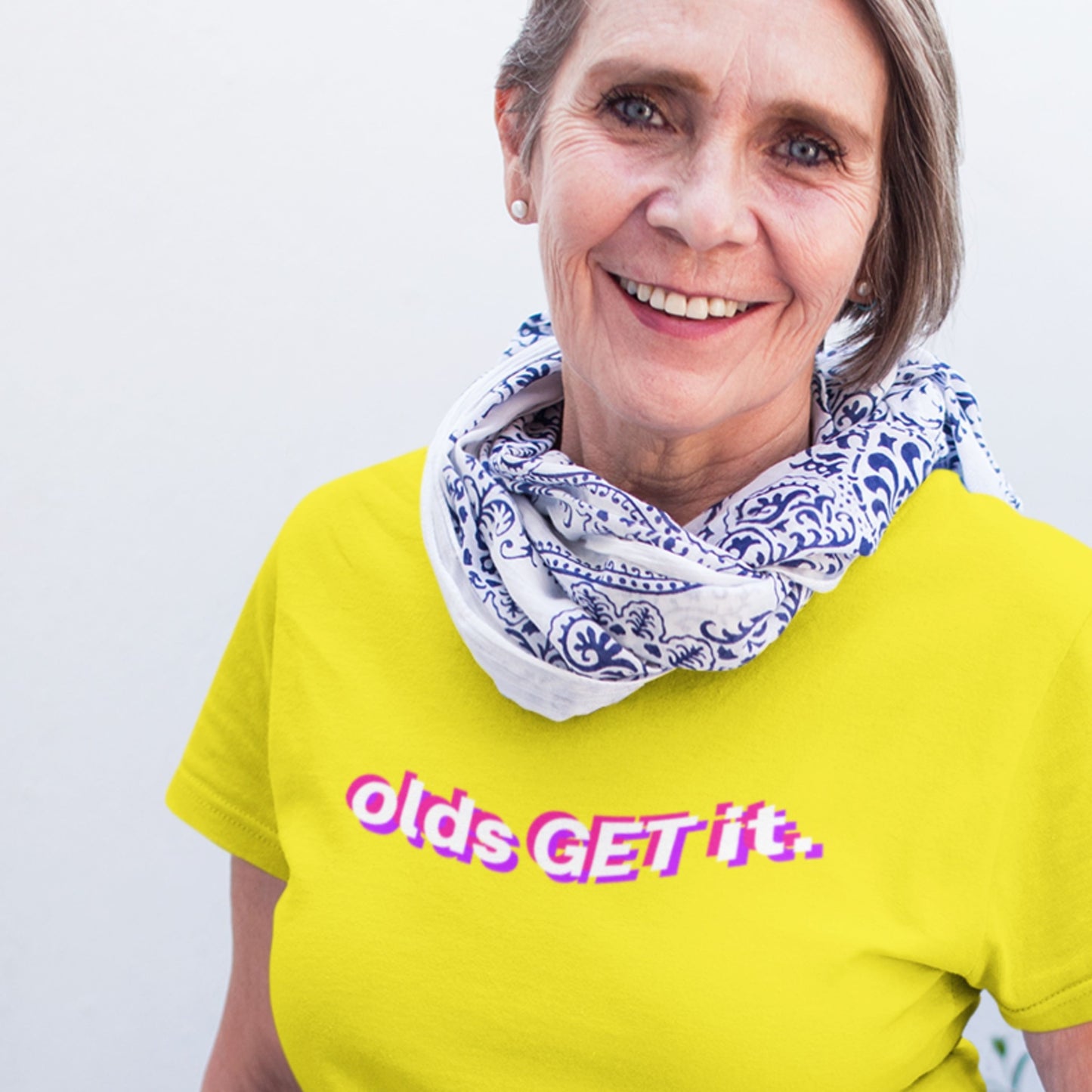 Woman wearing a yellow t-shirt with 'olds GET it.' text and a patterned scarf.