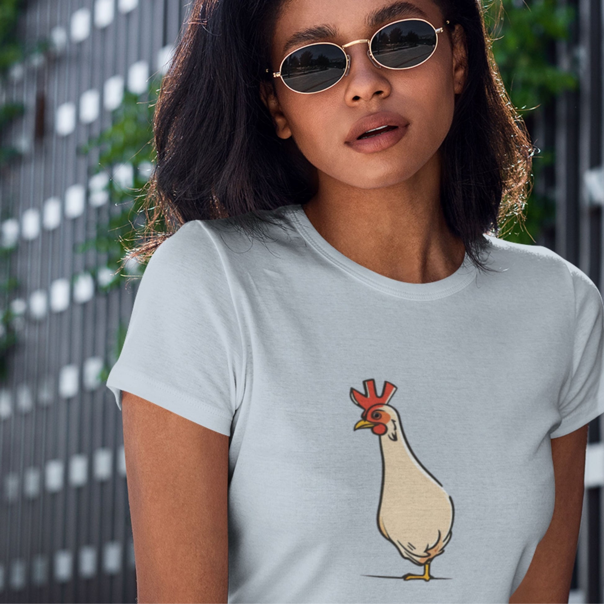 Light blue t-shirt with an illustration of a skinny chicken worn by a woman in sunglasses outside.