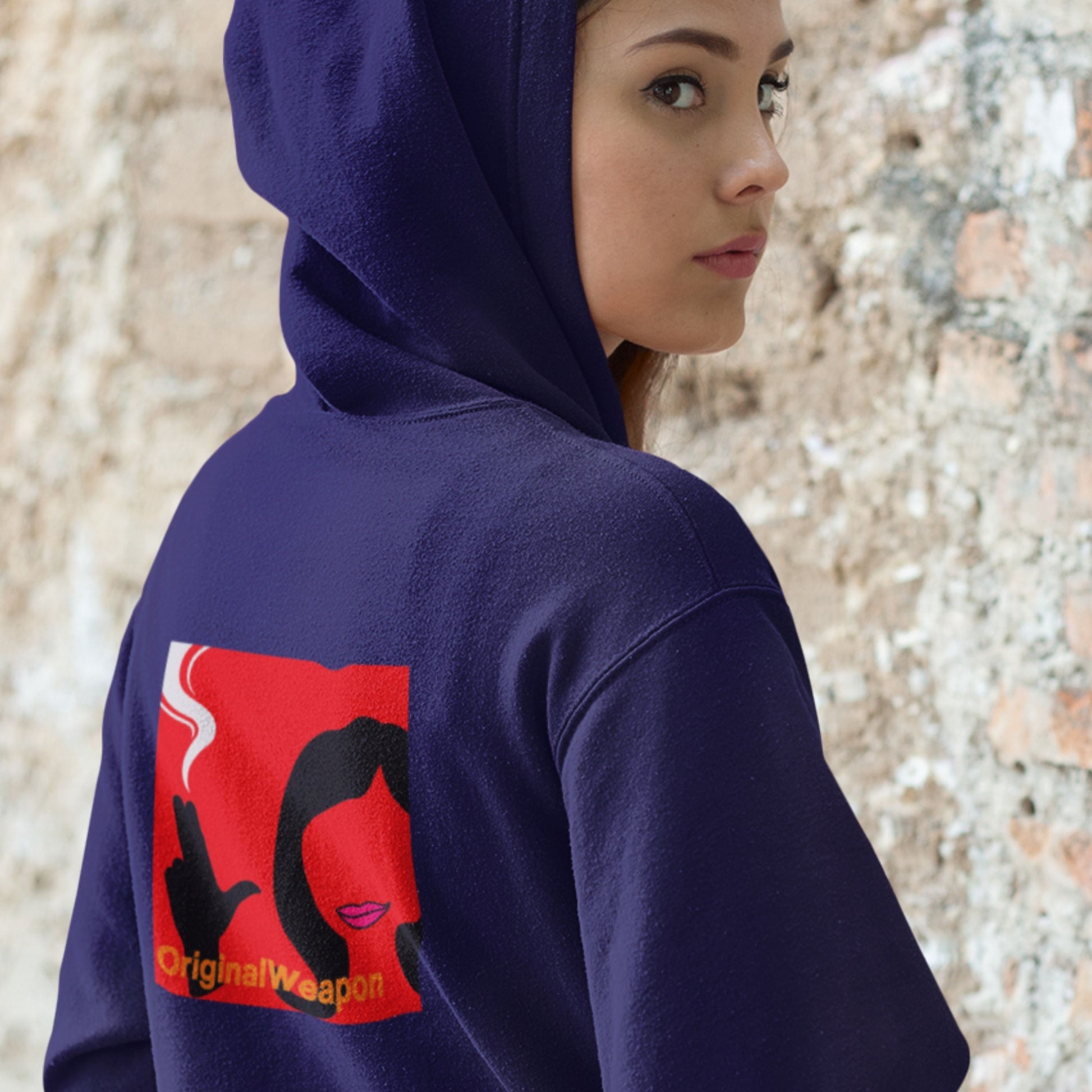 Person wearing a navy blue hoodie with a red and black design on the back, standing against a textured wall.