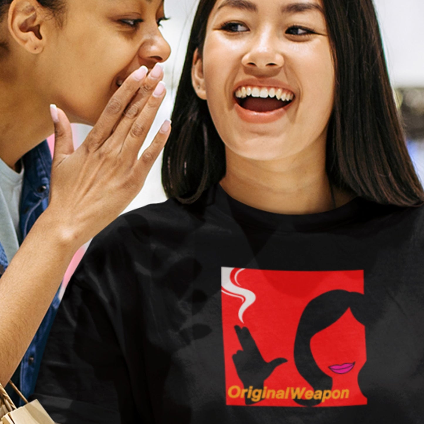 A model wearing a black t-shirt featuring the debut album cover for the pop group Original Weapon is being told a secret by her friend
