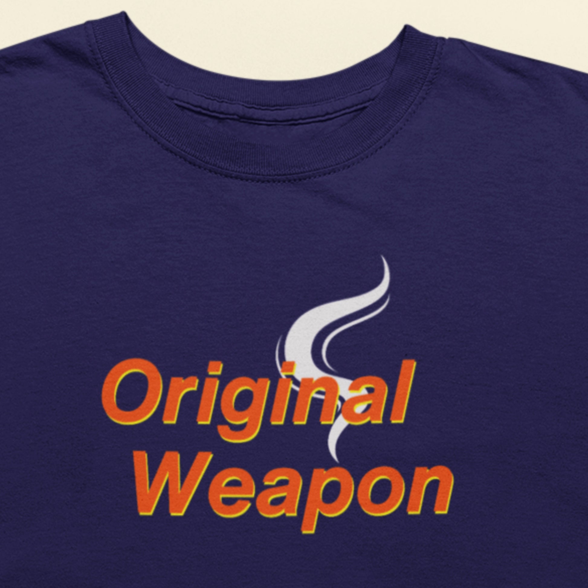 Navy blue t-shirt with 'Original Weapon' text and graphic on a beige background.