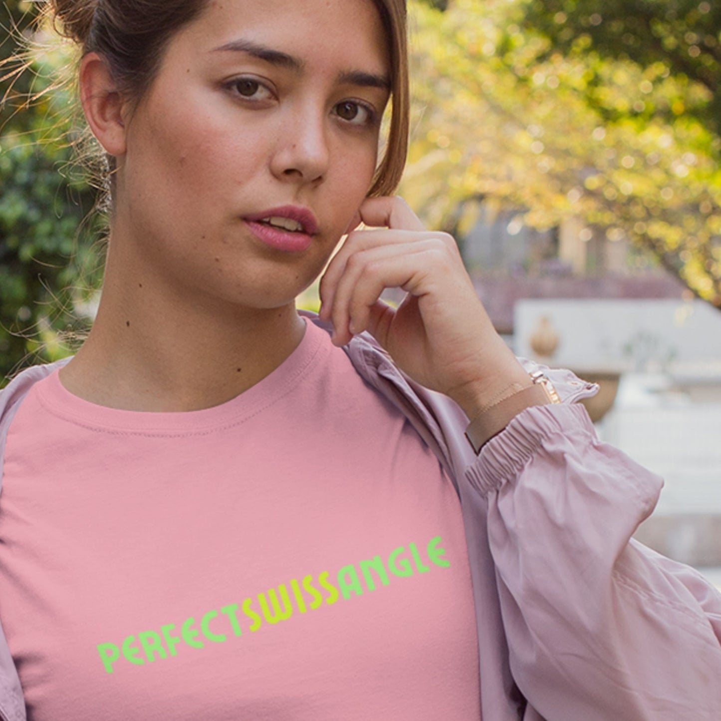 Woman wearing a pink shirt with 'PERFECTSWISSANGLE' text, standing outdoors.
