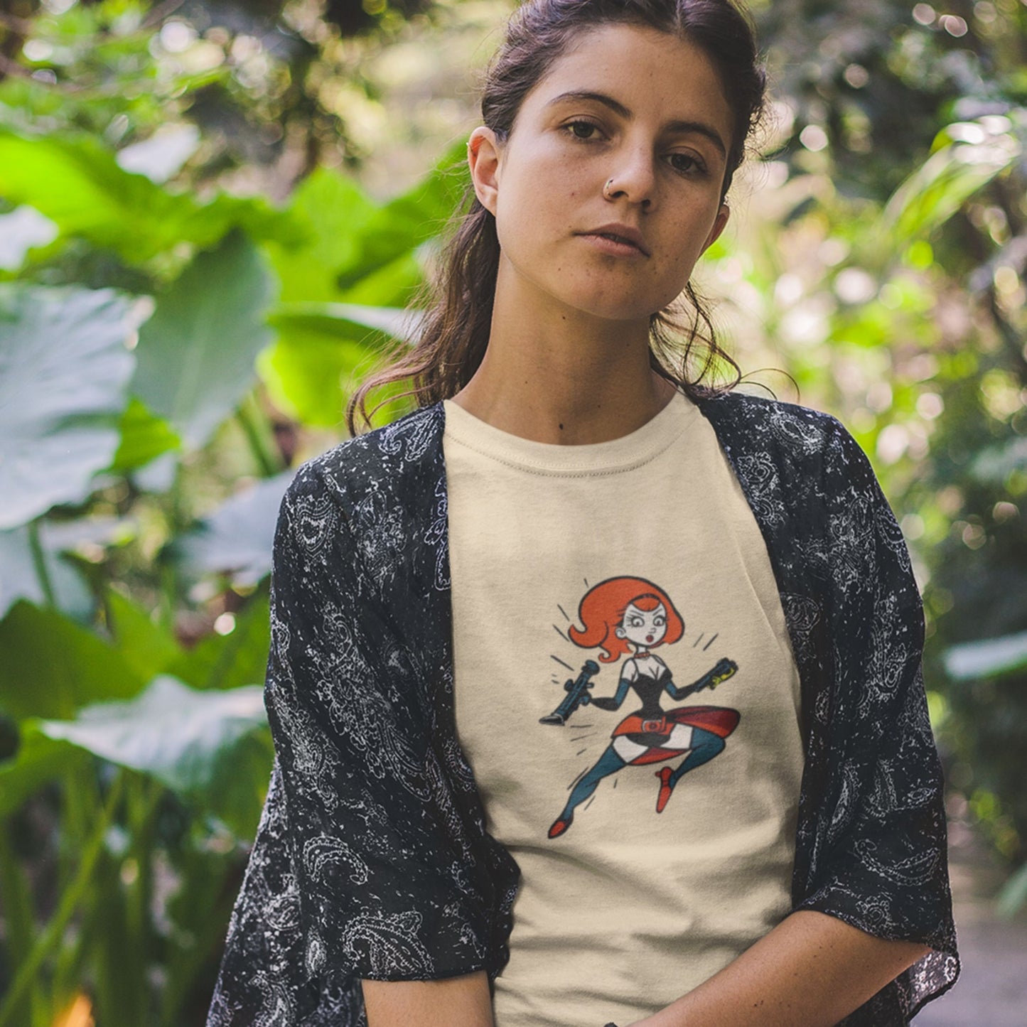 Woman wearing a beige t-shirt with a fun, colorful cartoon hero illustration in front of plants.