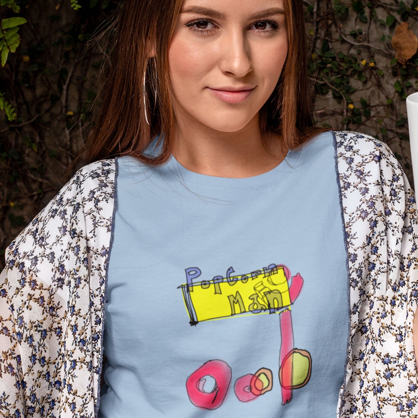 Woman wearing a baby blue t-shirt with a colorful abstract graffiti style drawing in a forest.