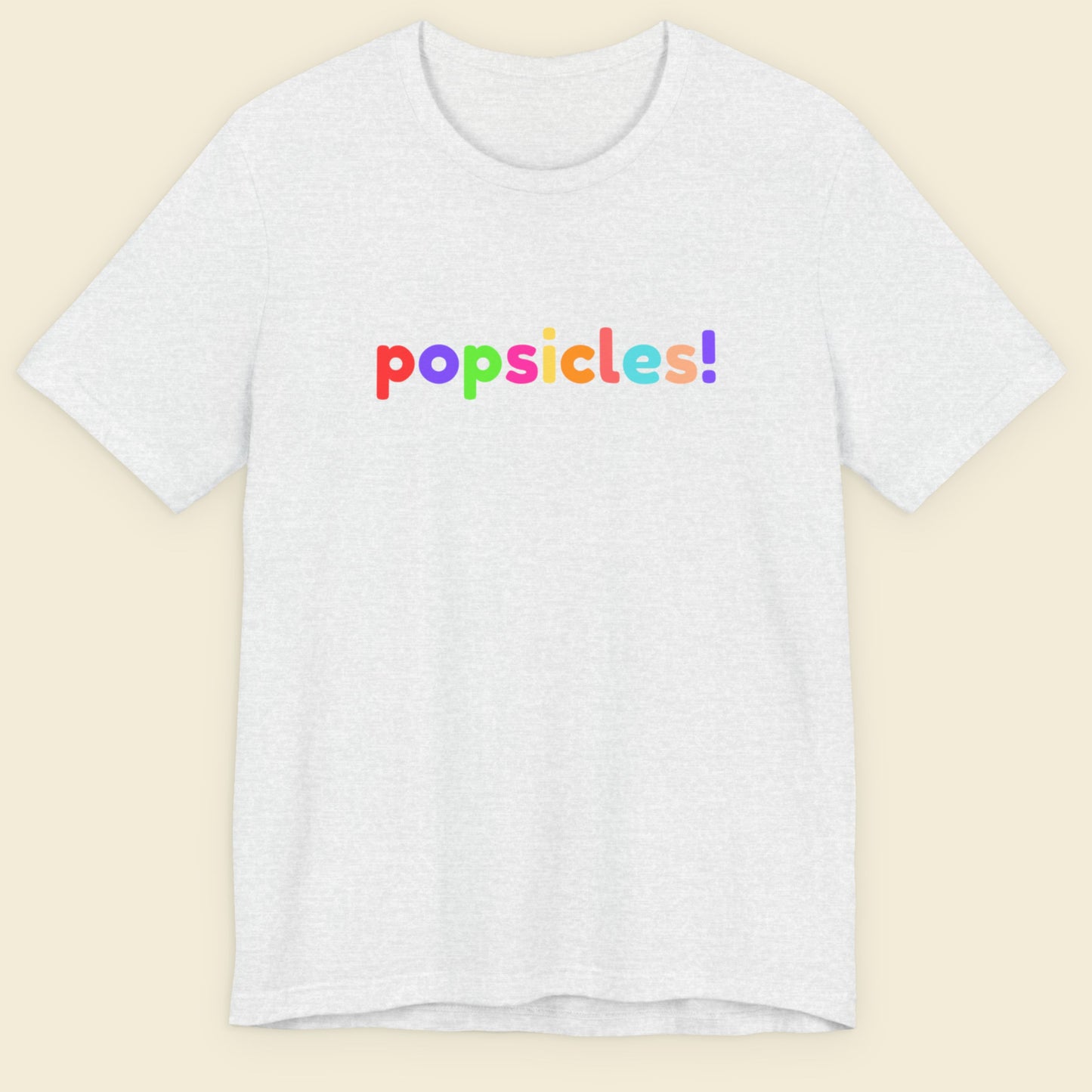 Ash grey t-shirt with 'popsicles!' text in colorful letters on a beige background