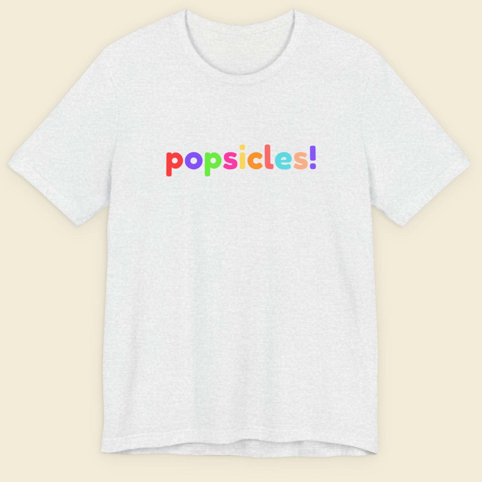 Ash grey t-shirt with 'popsicles!' text in colorful letters on a beige background